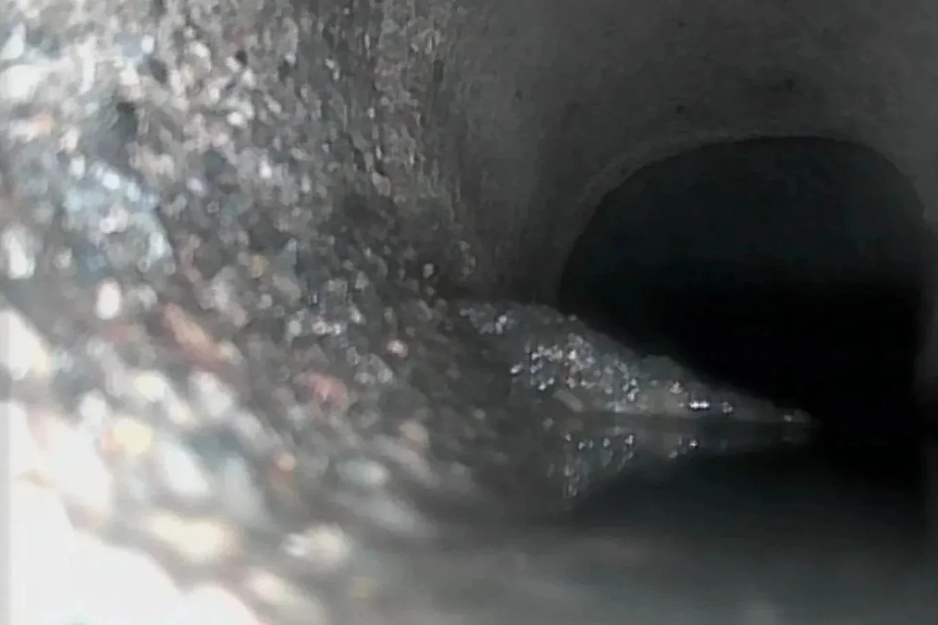 Close-up of a cast iron sewer pipe interior with a dark, round opening at the end.