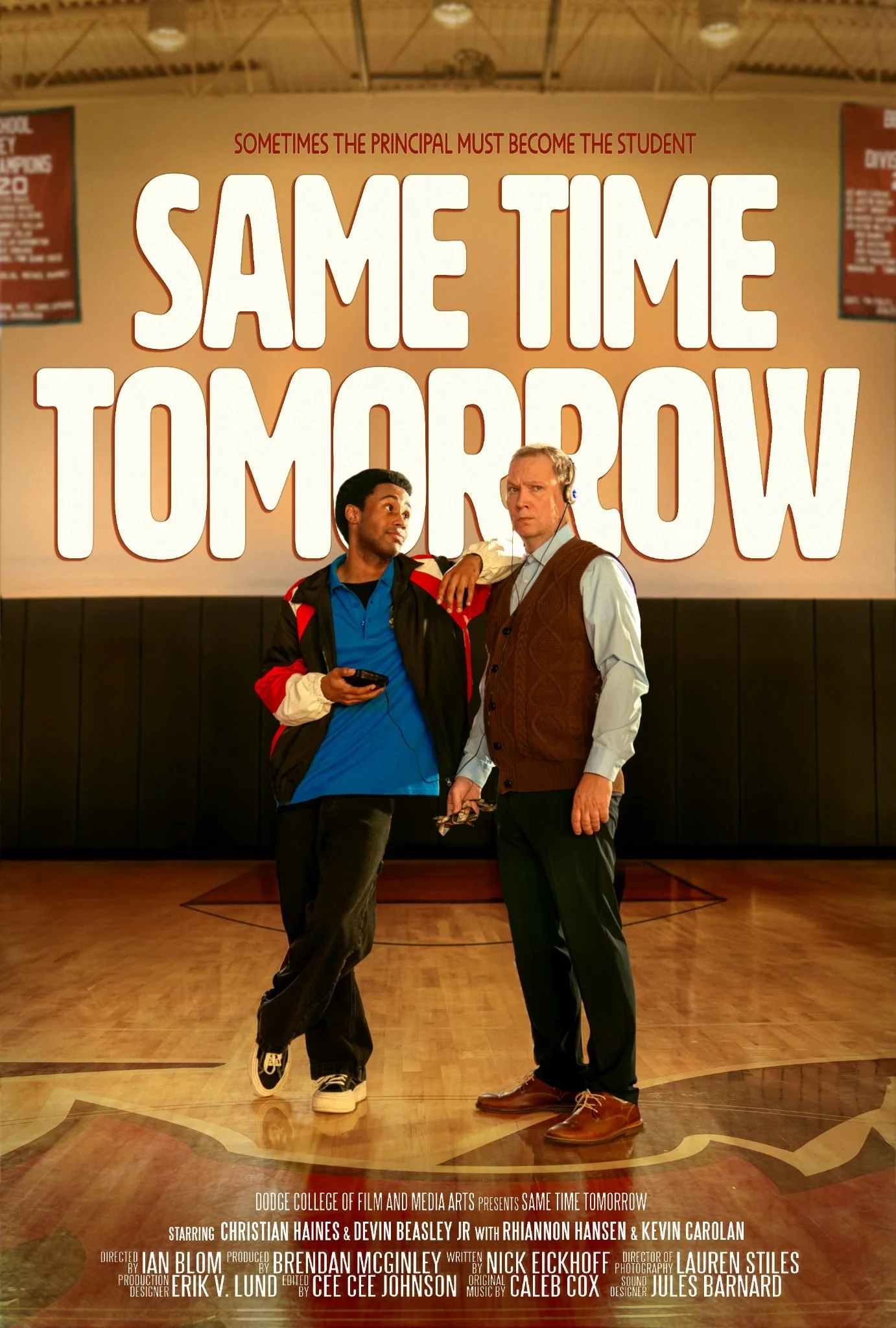 Two men standing in front of a large poster that reads "Sometimes the principal must become the student. Same Time Tomorrow." The men are in a gymnasium or auditorium with a polished wooden floor, and there are banners hanging from the ceiling.