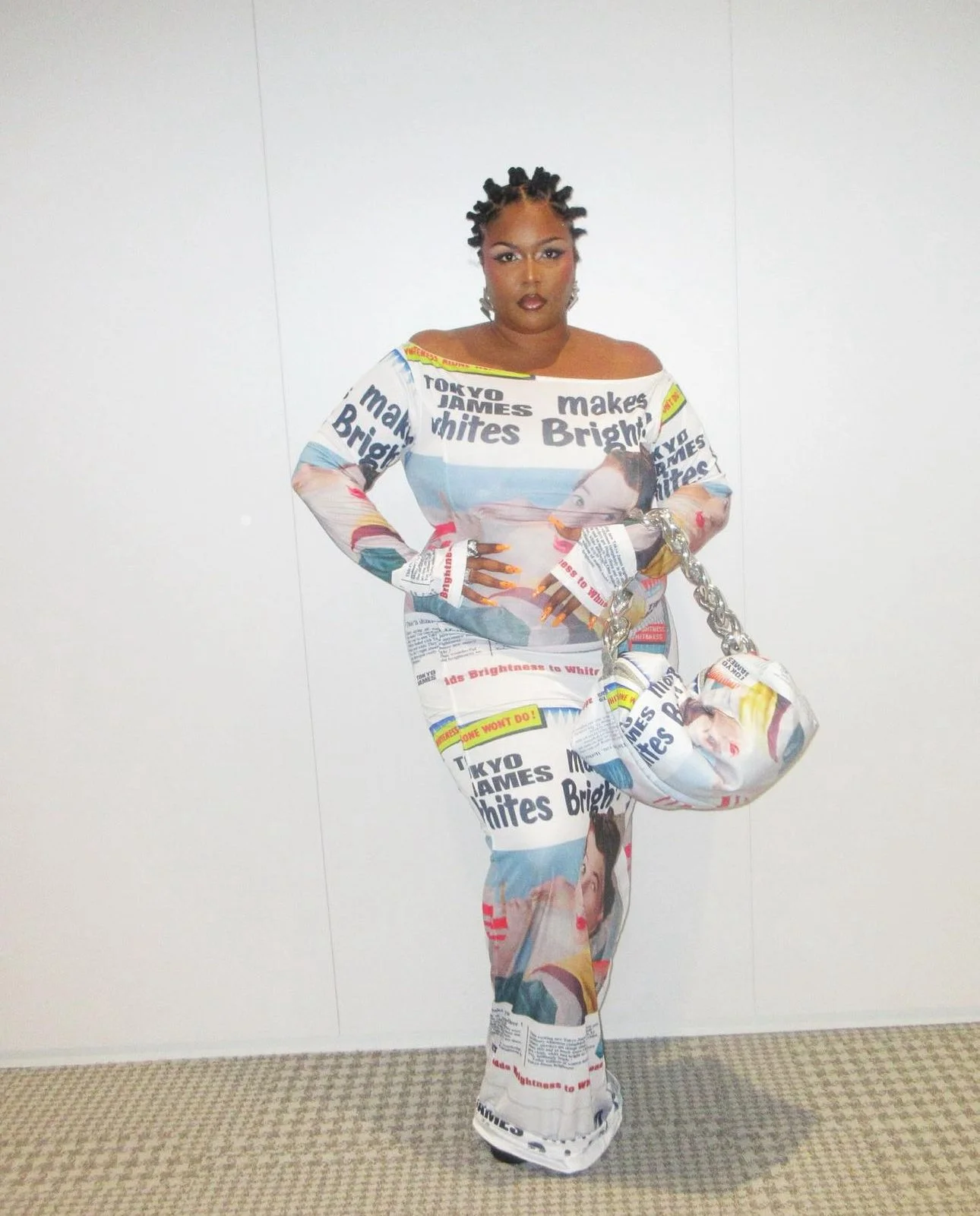 Woman dressed in a newspaper print outfit with a matching bag, posing against a plain white wall.