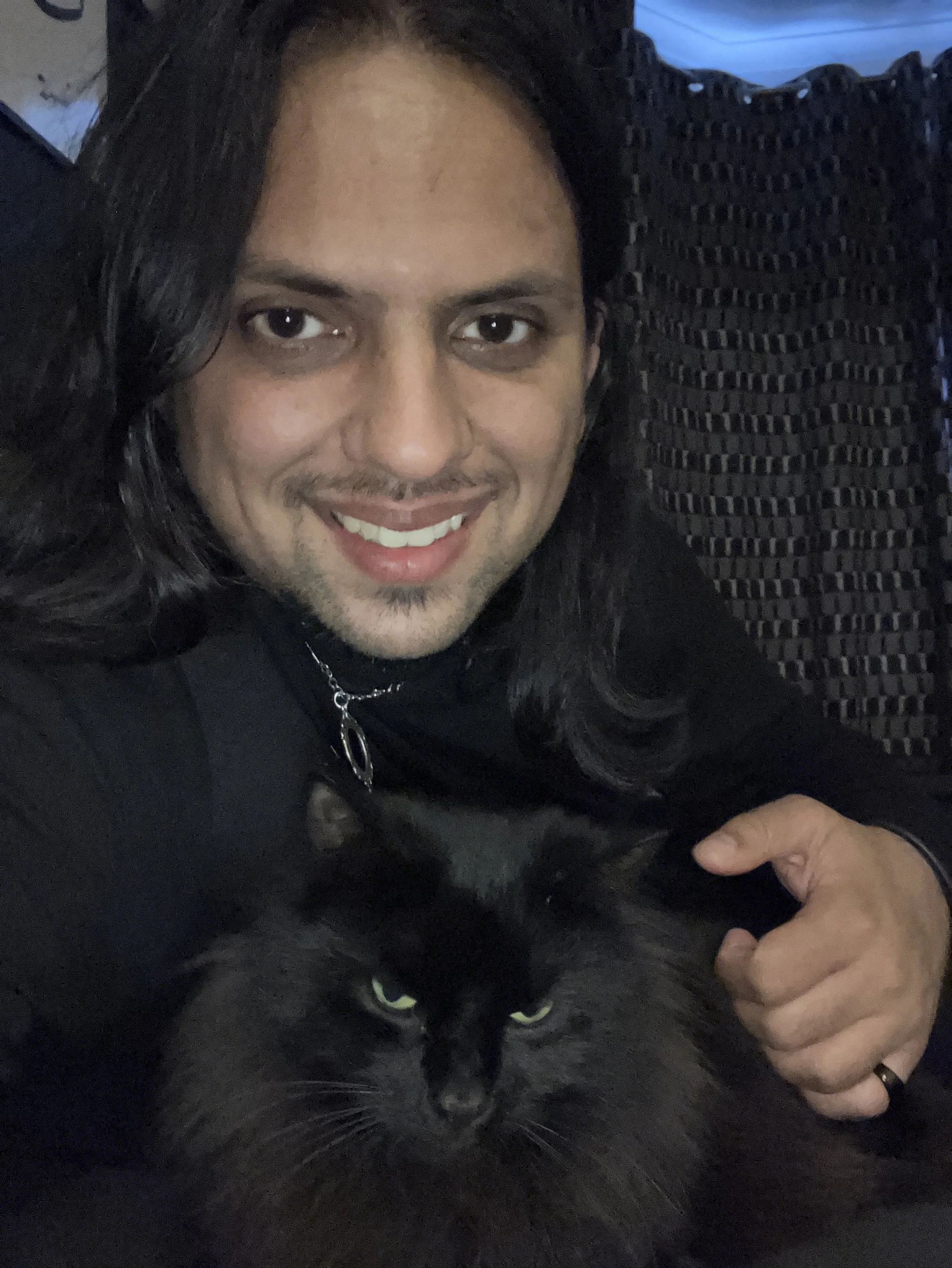 Man wearing black and holding a black cat with green eyes.