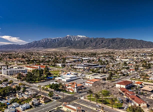 A cityscape with a mountain range in the background, snow-capped peaks, and a clear blue sky.