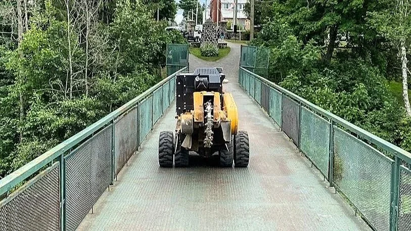 Small construction vehicle on a pedestrian bridge, surrounded by trees and greenery.