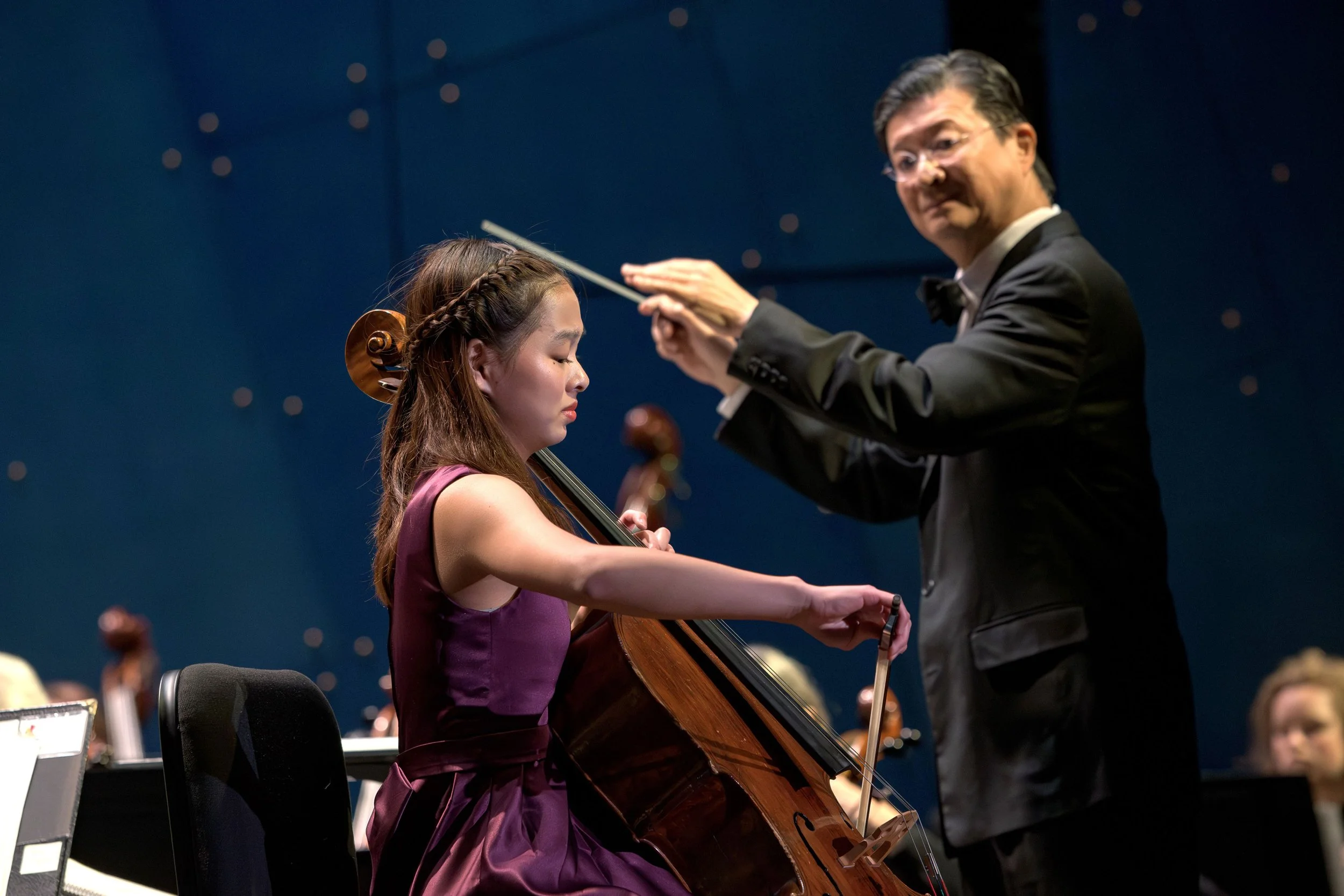 Conductor directs a young woman playing the cello during a concert on stage.