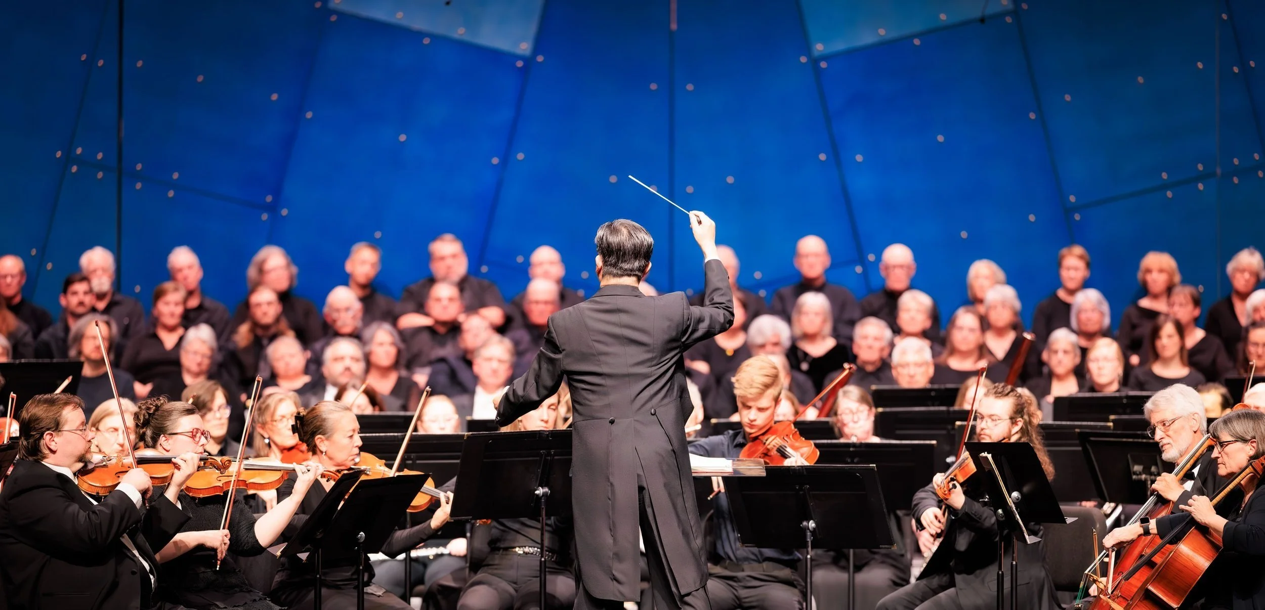 Orchestra performing with a conductor on stage against a blue backdrop.