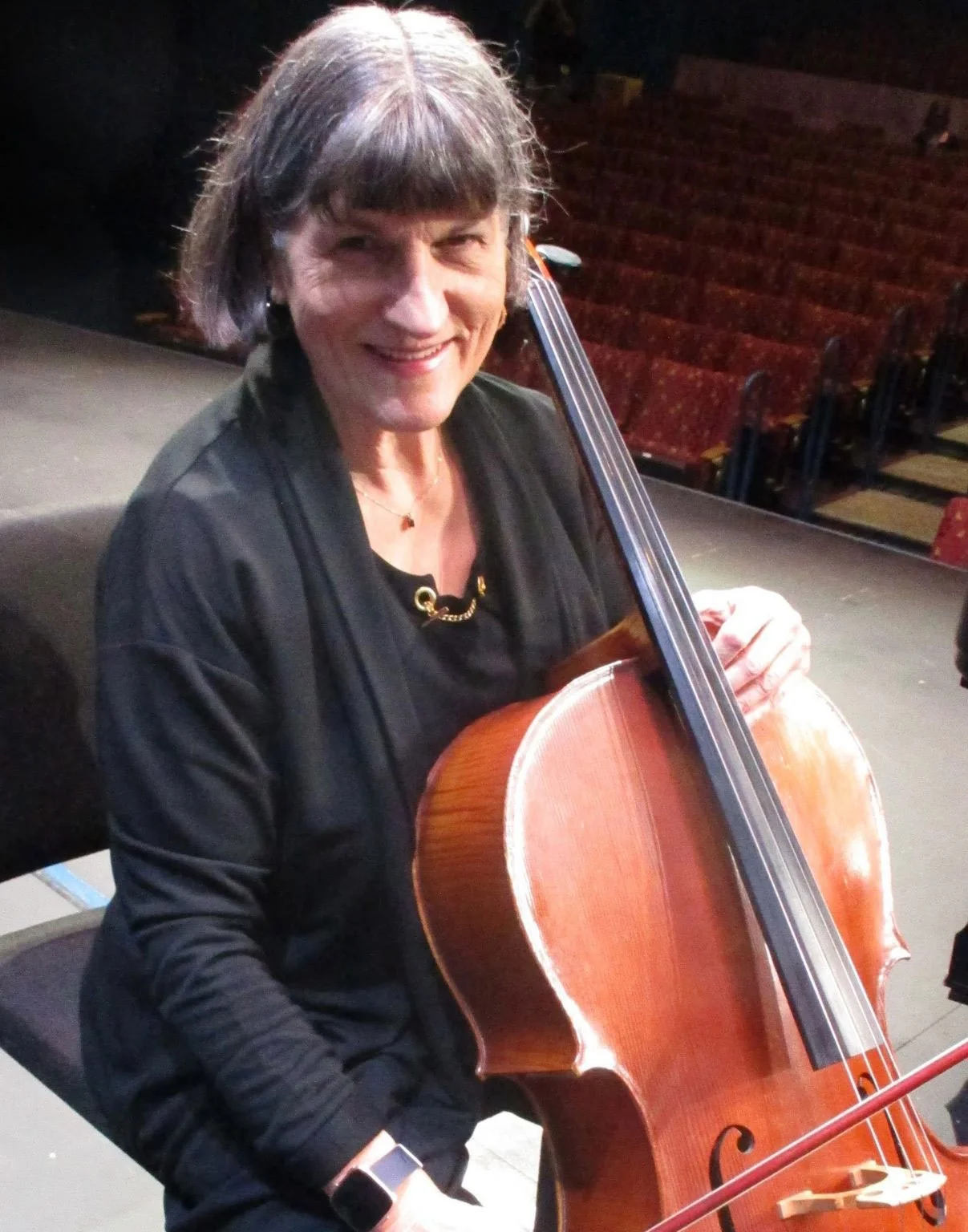 Woman playing the cello on a stage, smiling at the camera.
