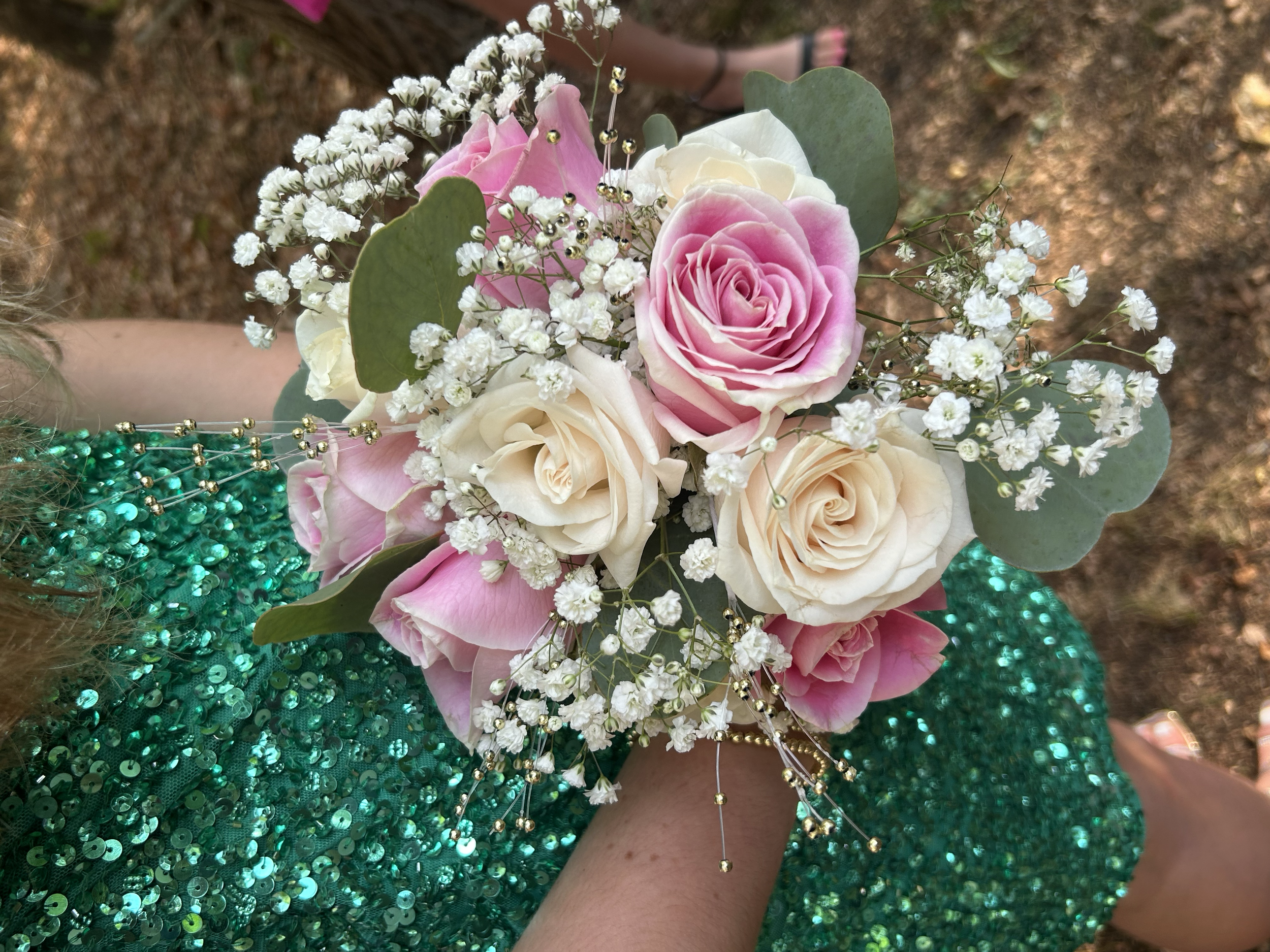 A person wearing a green sequined dress holds a bouquet of pink and white roses, baby's breath, and eucalyptus leaves.