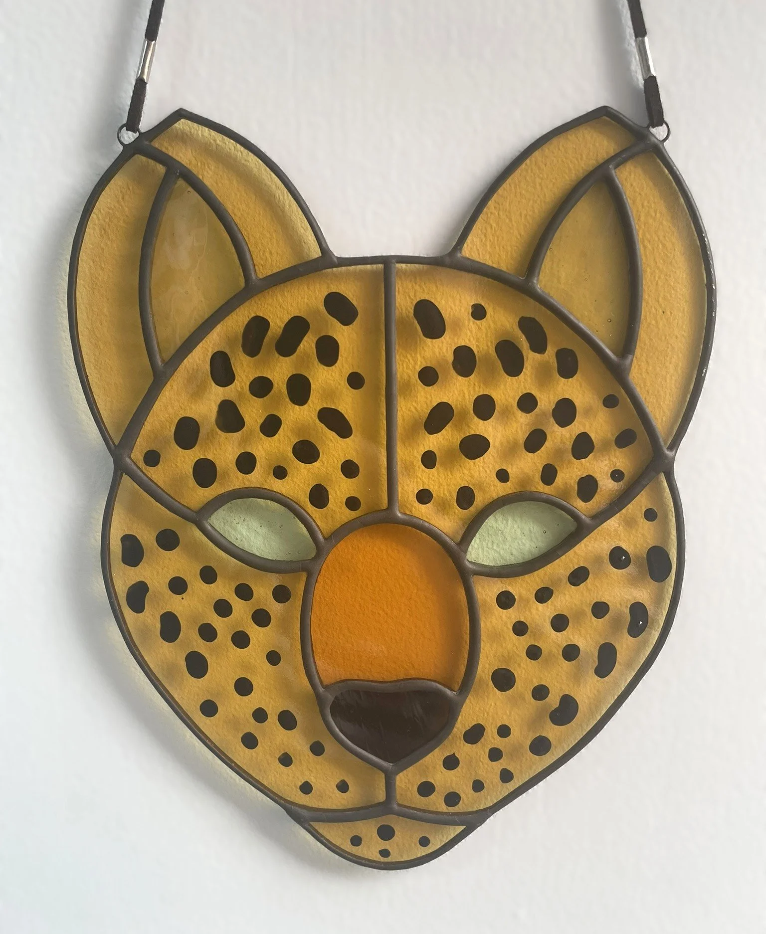 Crafted Colours commission of a leopard face in stained glass. The leopard is seen face on and comprises multiple shades of yellow and amber with black spots.