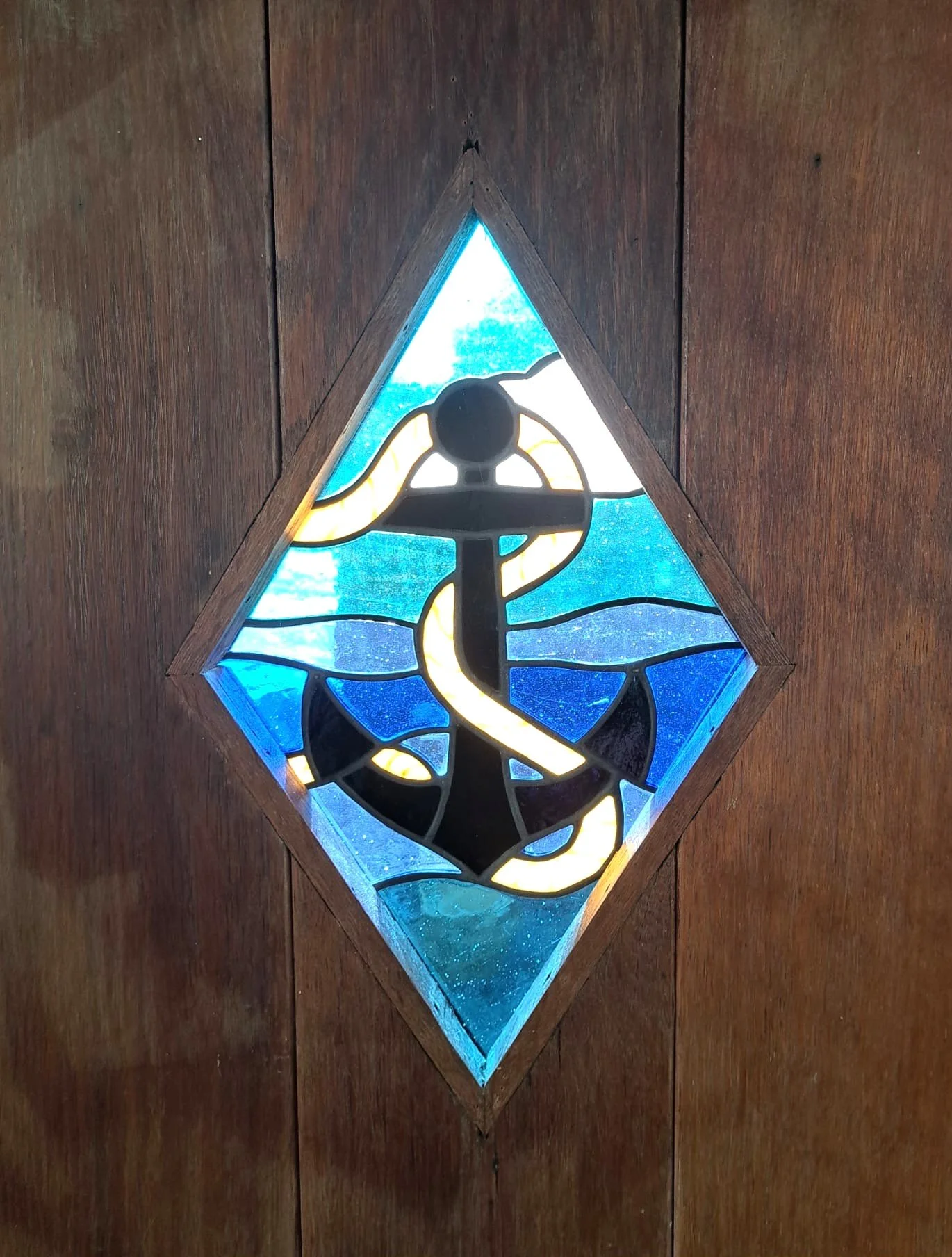 Crafted Colours commission of a diamond shape stained glass panel featuring a rope fouled anchor with sea and sky in the background set in a wood door