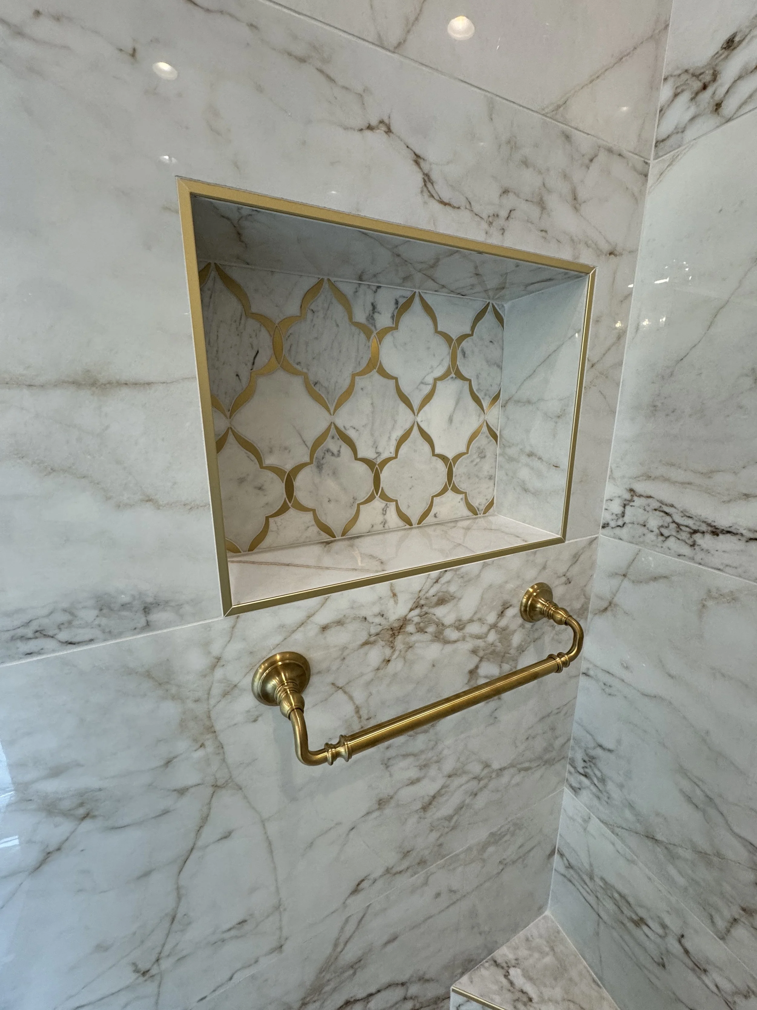 Marble wall with a built-in shelf or niche decorated with gold trim, gold piping, and patterned tile inside.