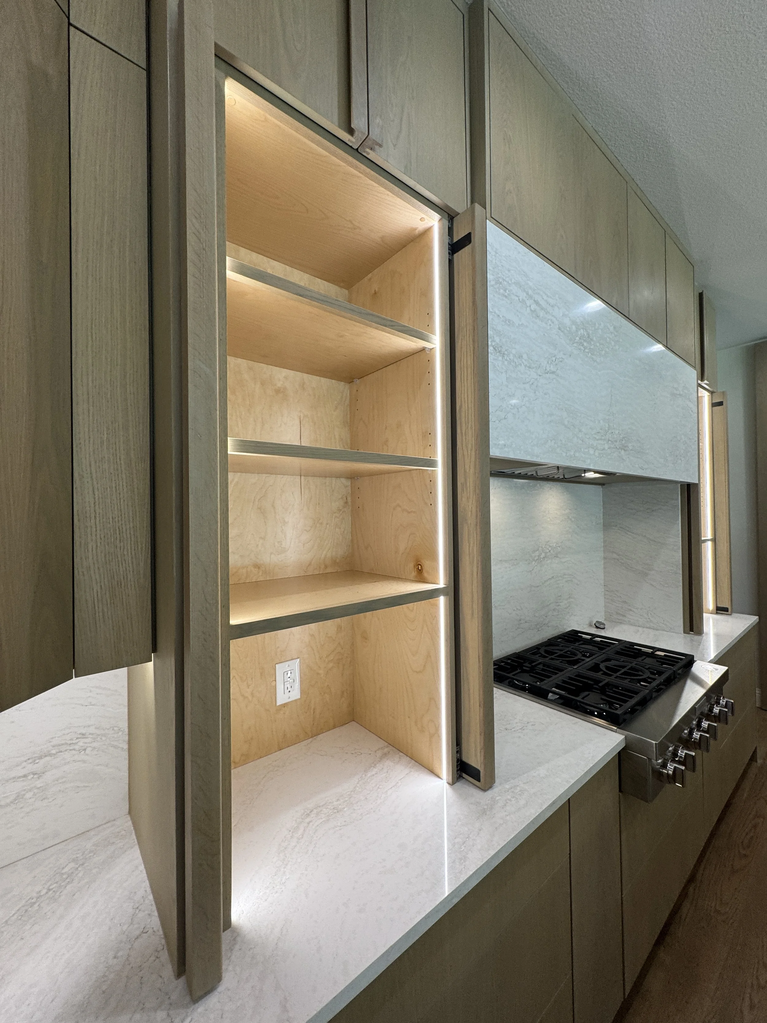 Unfinished kitchen with open shelving, light wood cabinets, a white countertop, and a black stovetop.