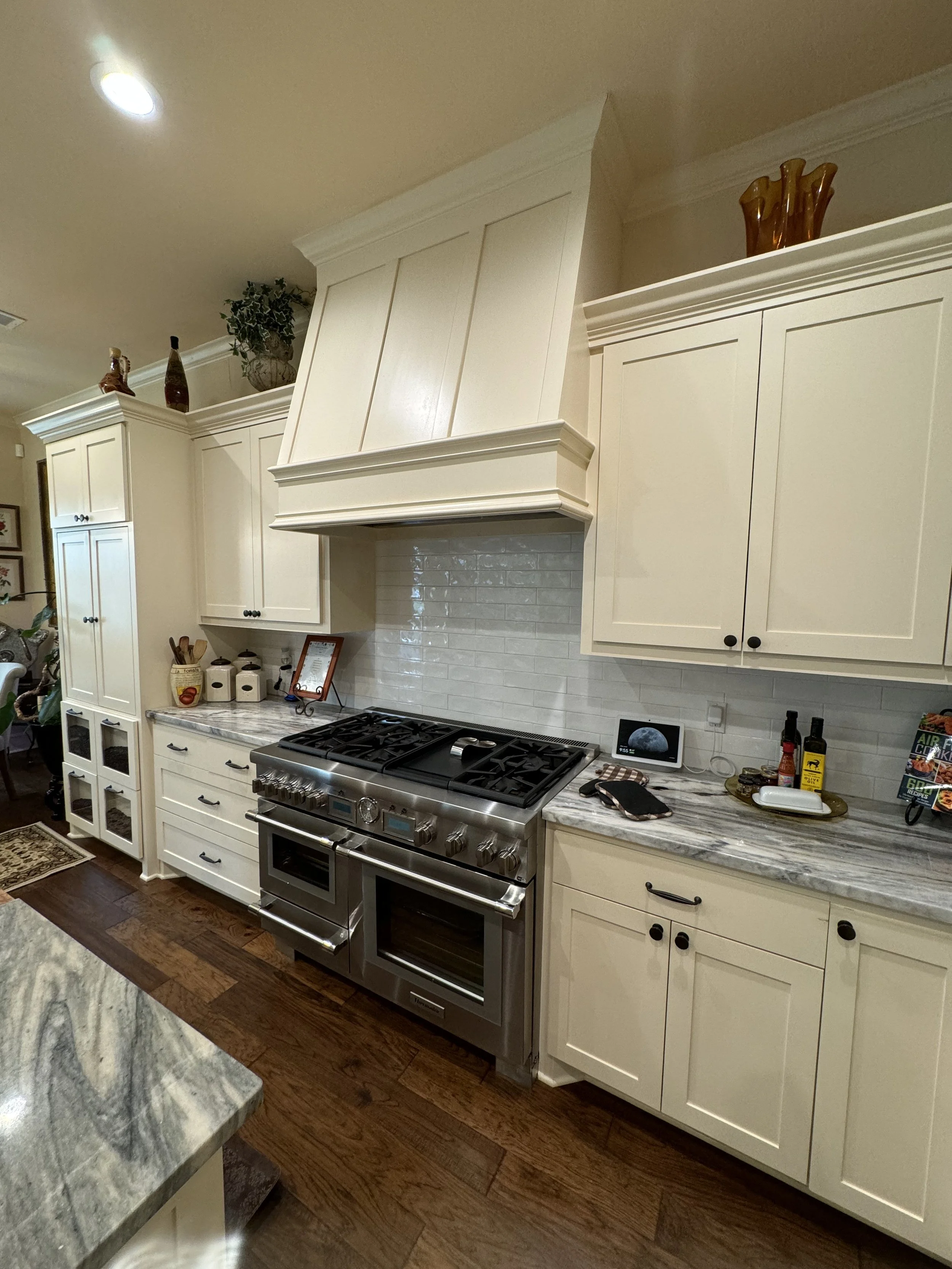 Kitchen with white cabinets, marble countertop, stainless steel stove, and decorative items on top of the cabinets.