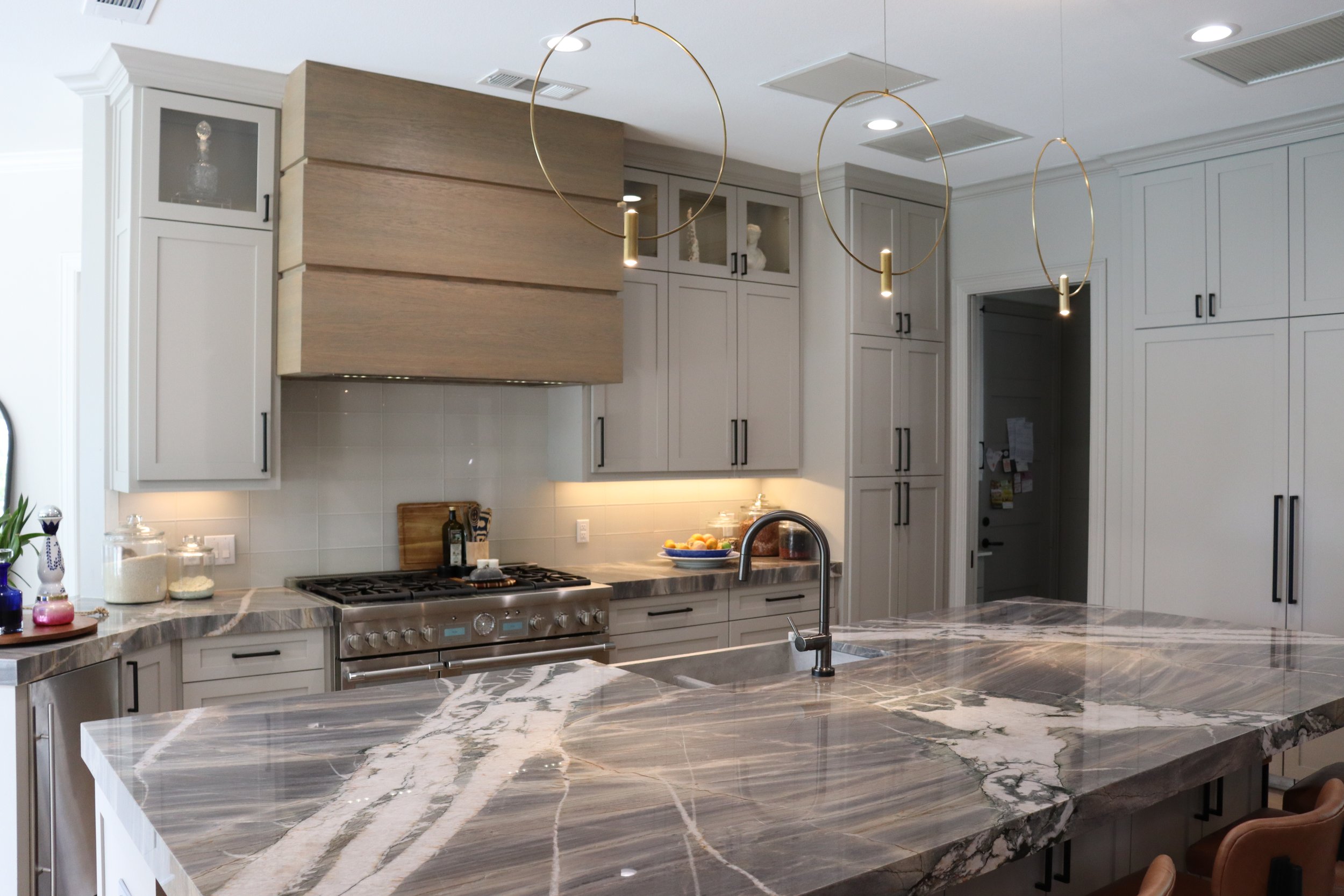 A modern kitchen with white and light wood cabinets, a marble countertop, and gold pendant lights hanging above a kitchen island.