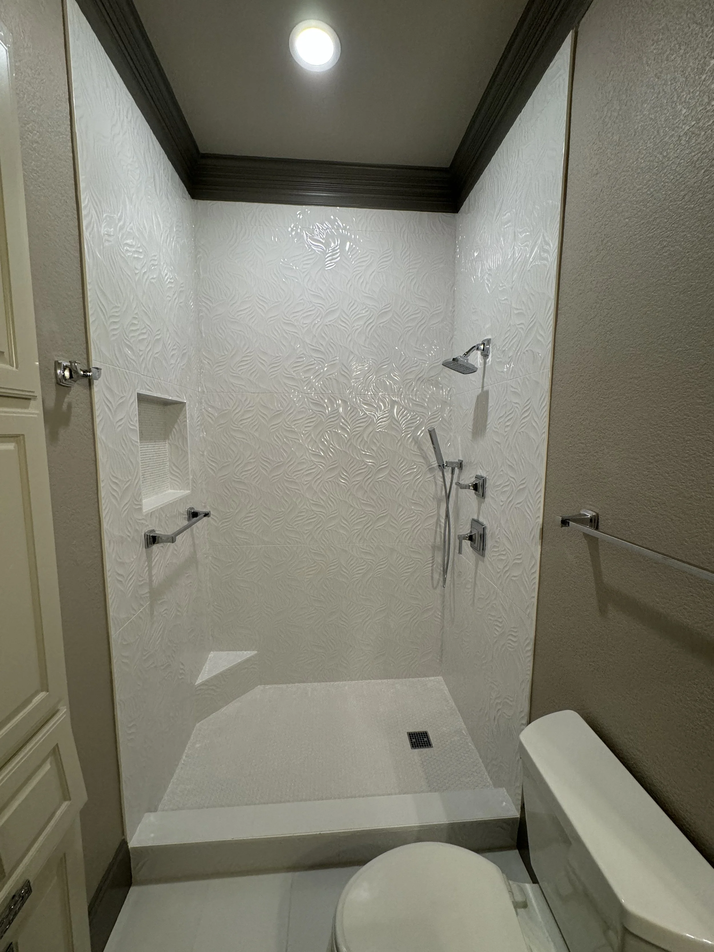 Bathroom with a walk-in shower, white textured tile walls, a black ceiling trim, a ceiling light, and a toilet.