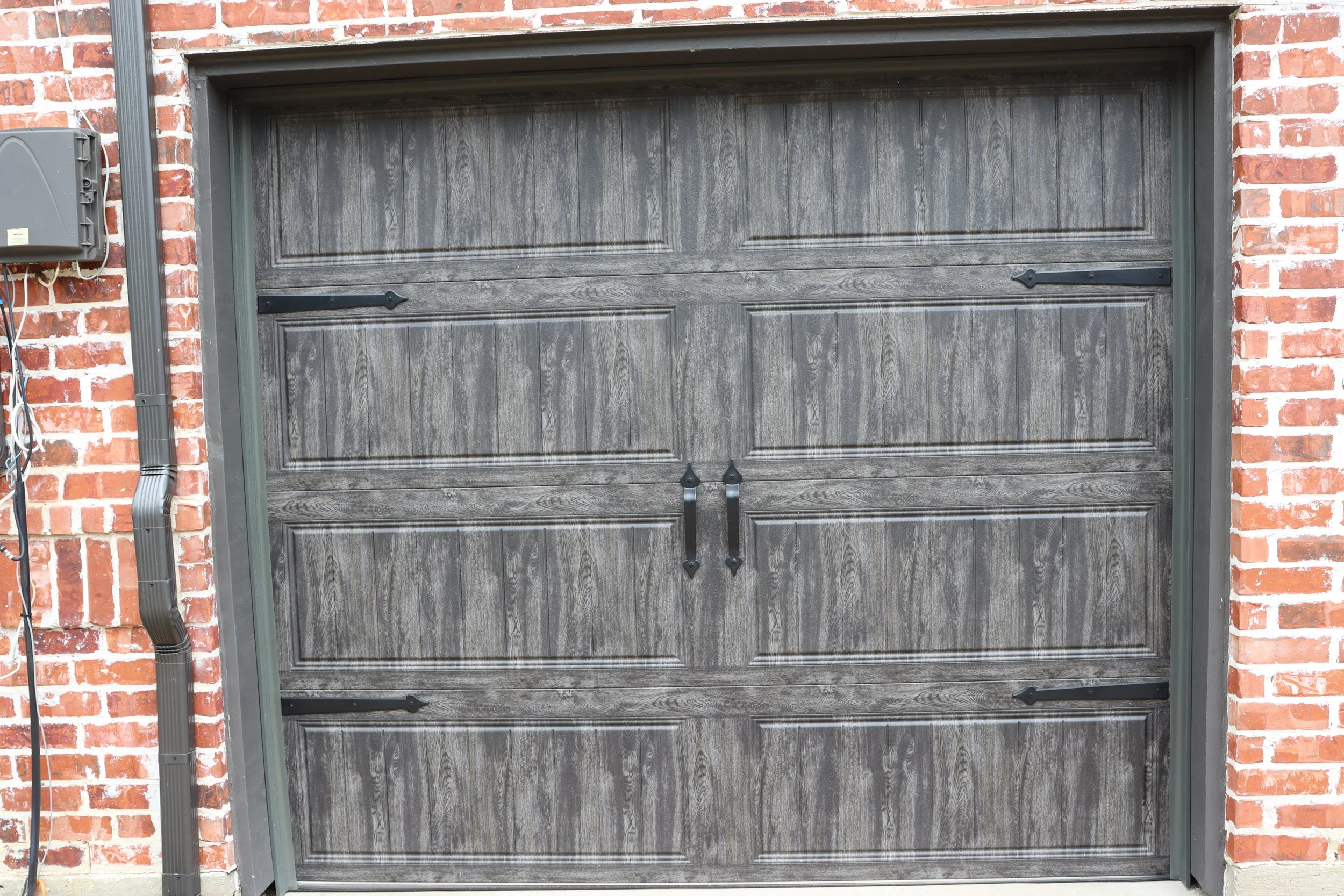 A gray wooden garage door set in a red brick building with black hardware and black trim.