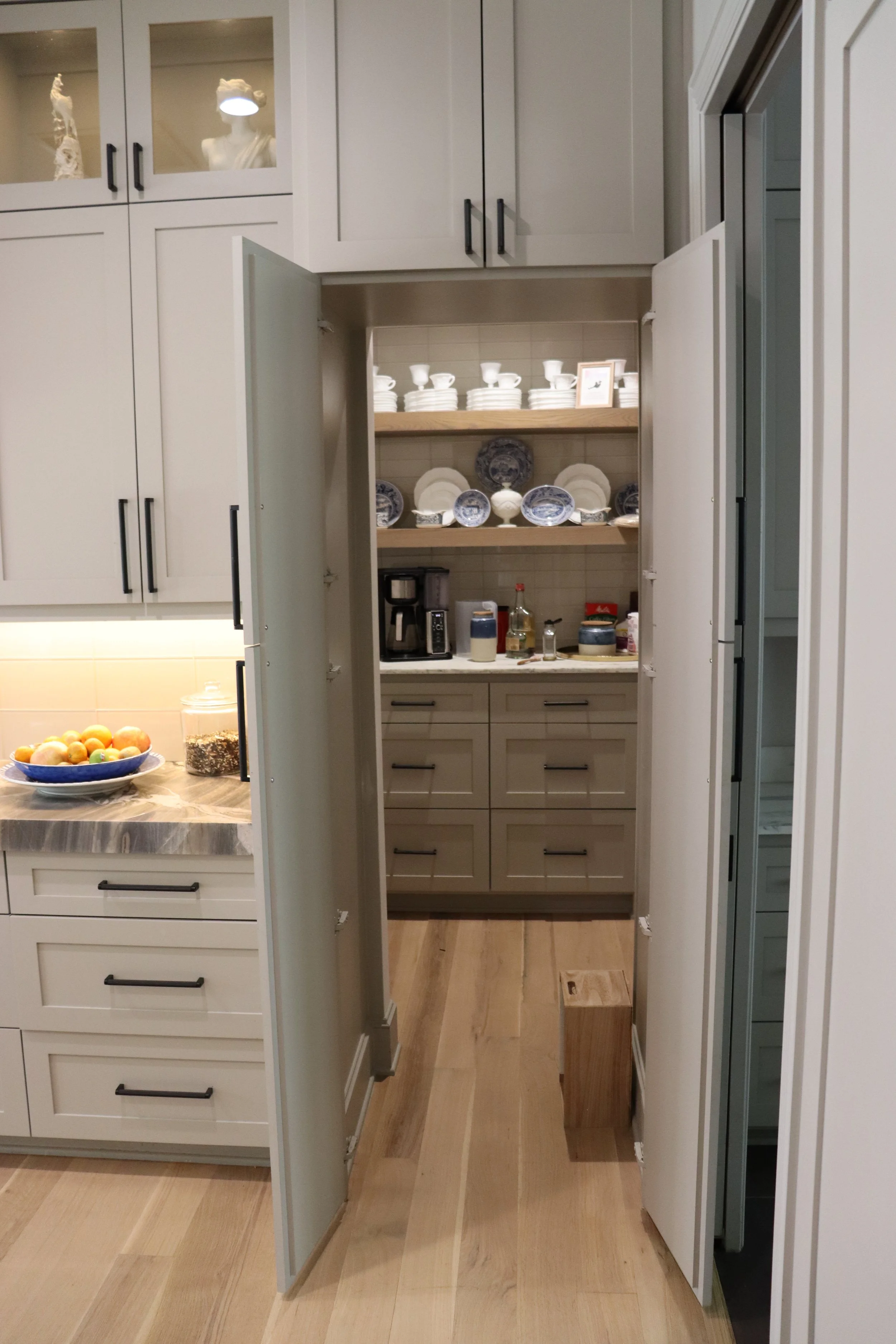 View of an open pantry with neatly arranged dishes and kitchen items inside, adjacent to kitchen cabinets.