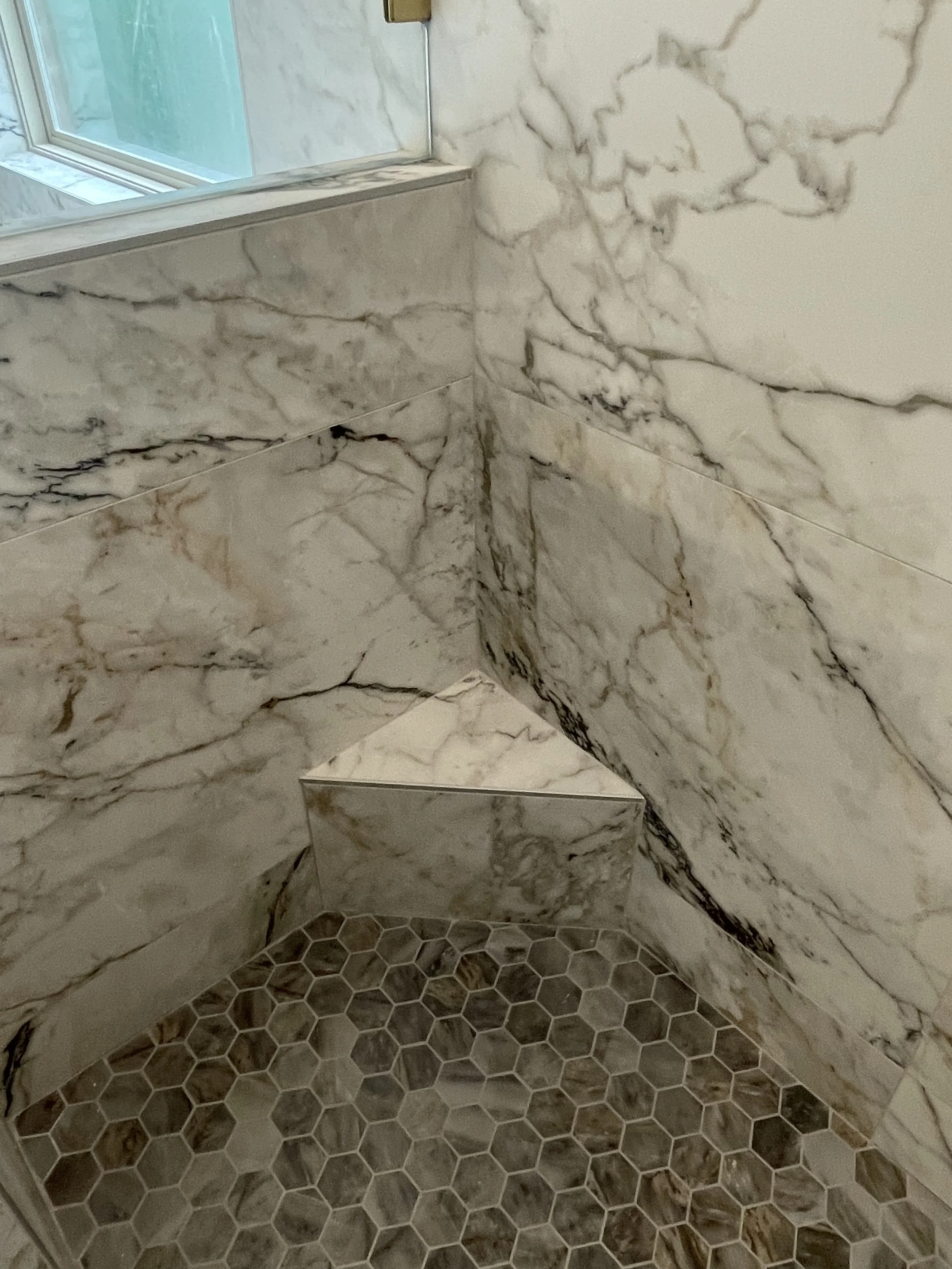 Bathroom corner with marble walls and hexagonal tile floor.