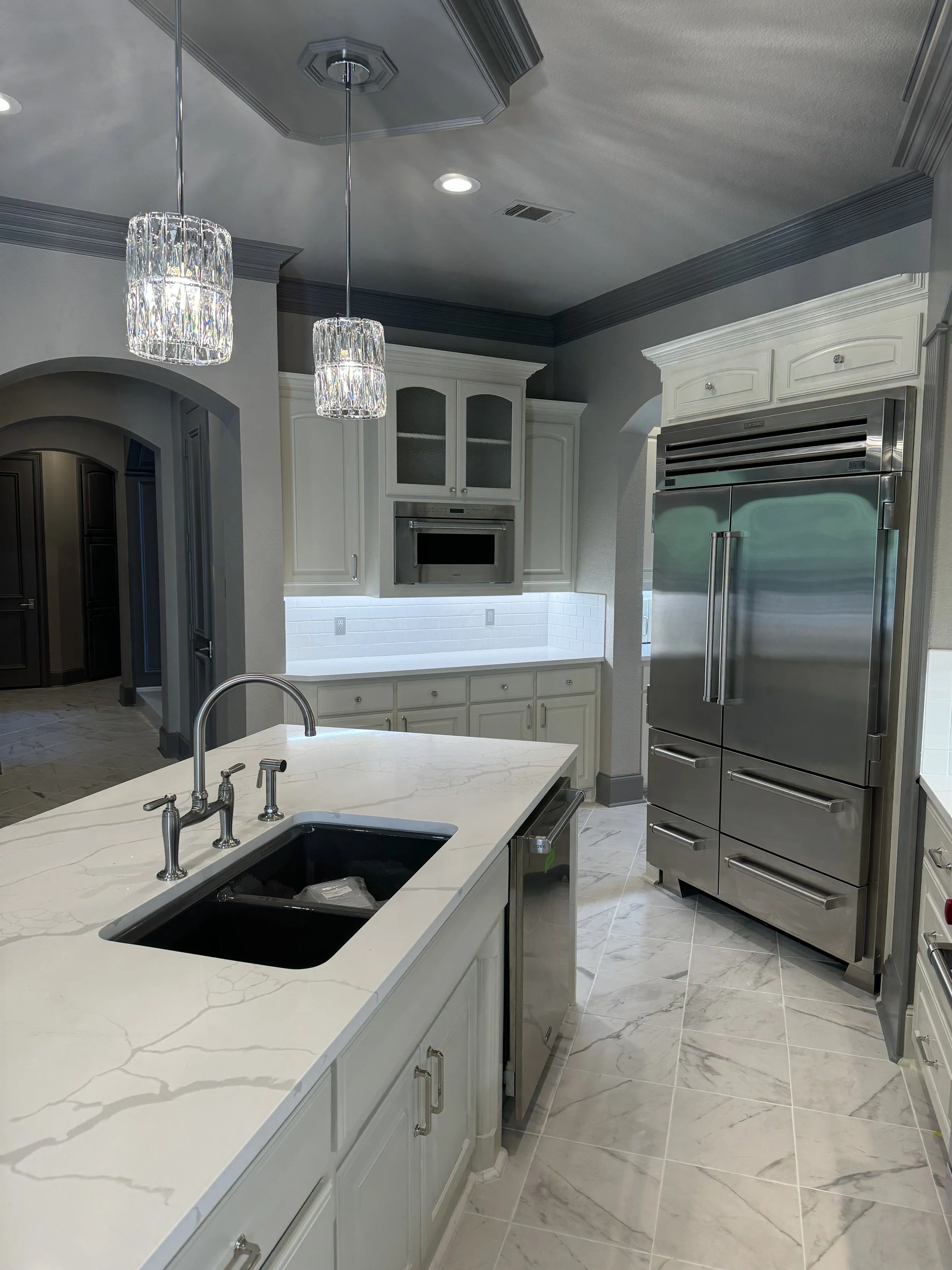 Modern kitchen with white cabinets, a marble island with a black sink, stainless steel appliances, and two crystal pendant lights hanging from the ceiling.