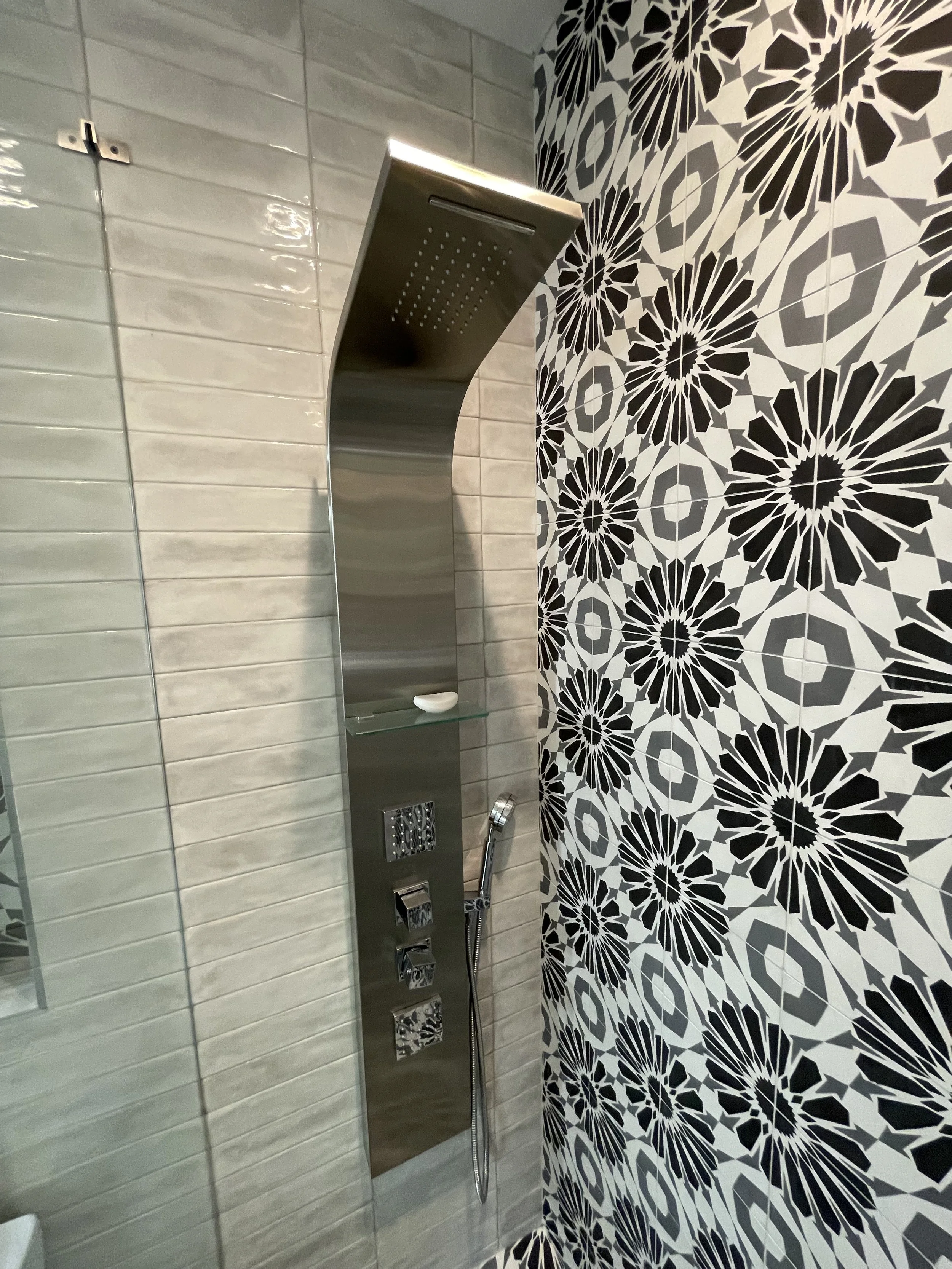 Modern shower with a stainless steel rainfall showerhead, a handheld shower, and decorative black and white floral patterned wall tiles.