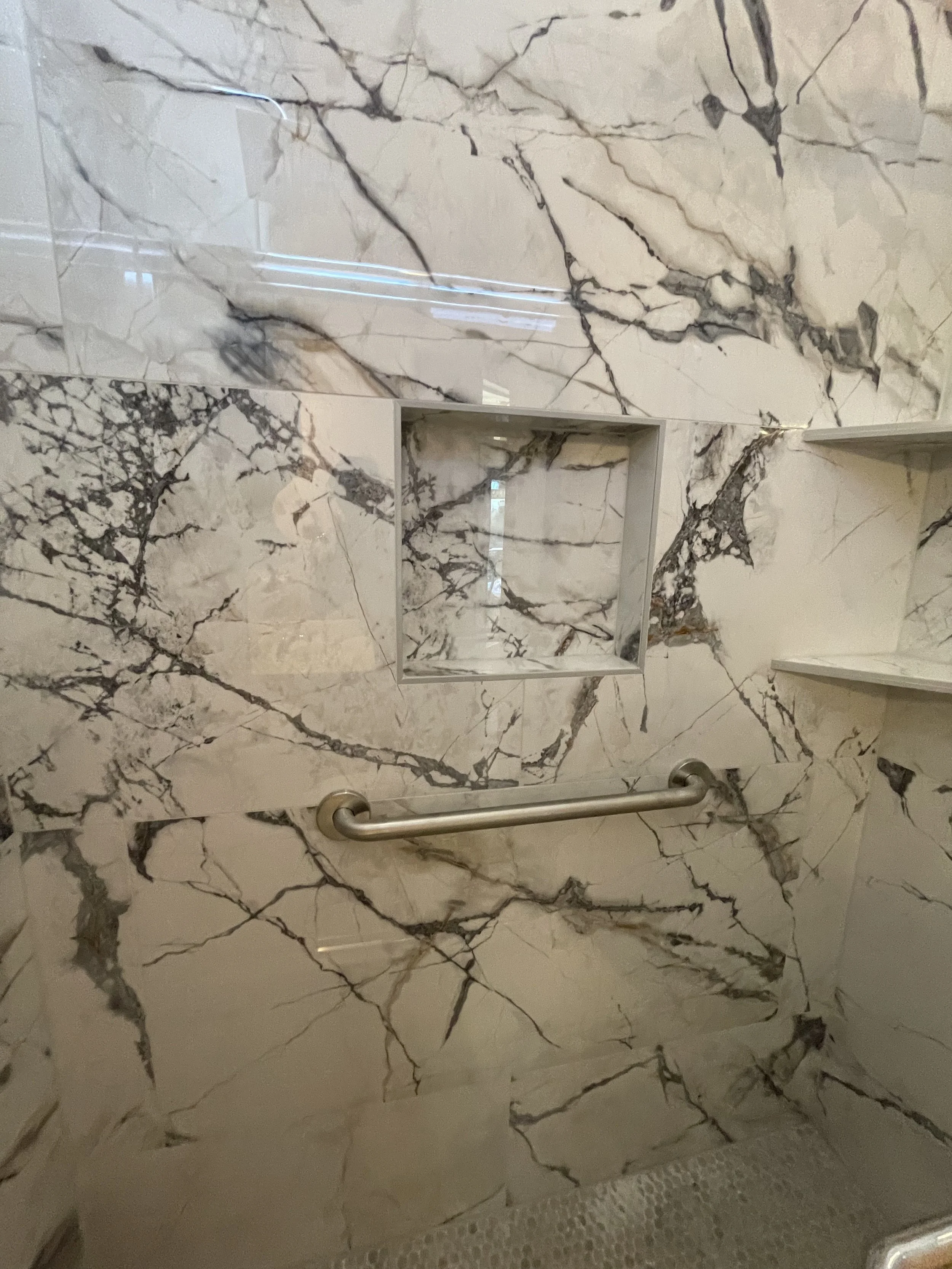 Marble wall with dark veining and a small recessed shelf, with a metal handrail visible below.