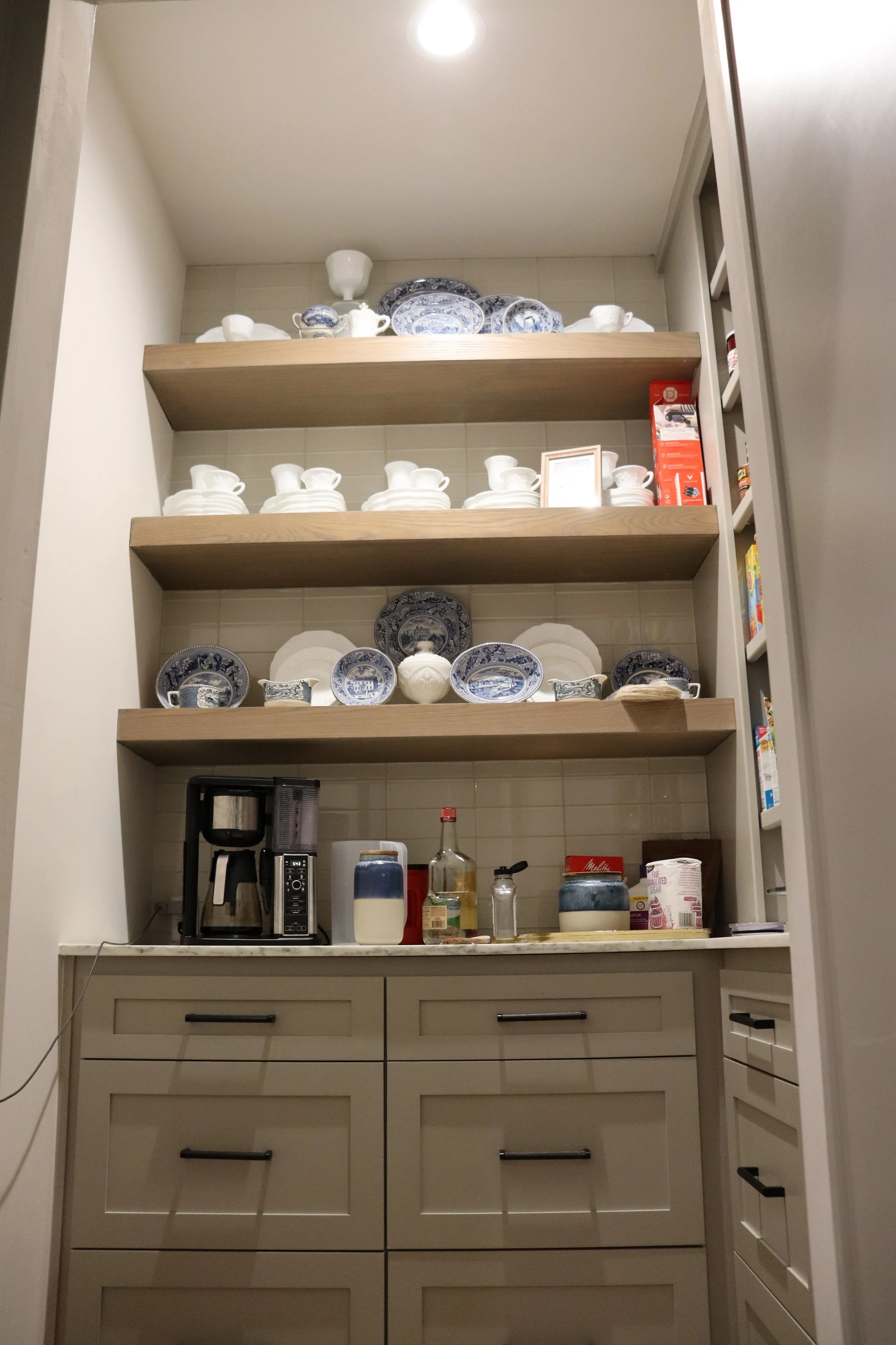 A kitchen pantry shelf with blue and white dishware including plates and teacups, some stacked. The lower part of a kitchen counter with various appliances and containers, including a coffee maker, and kitchen supplies.