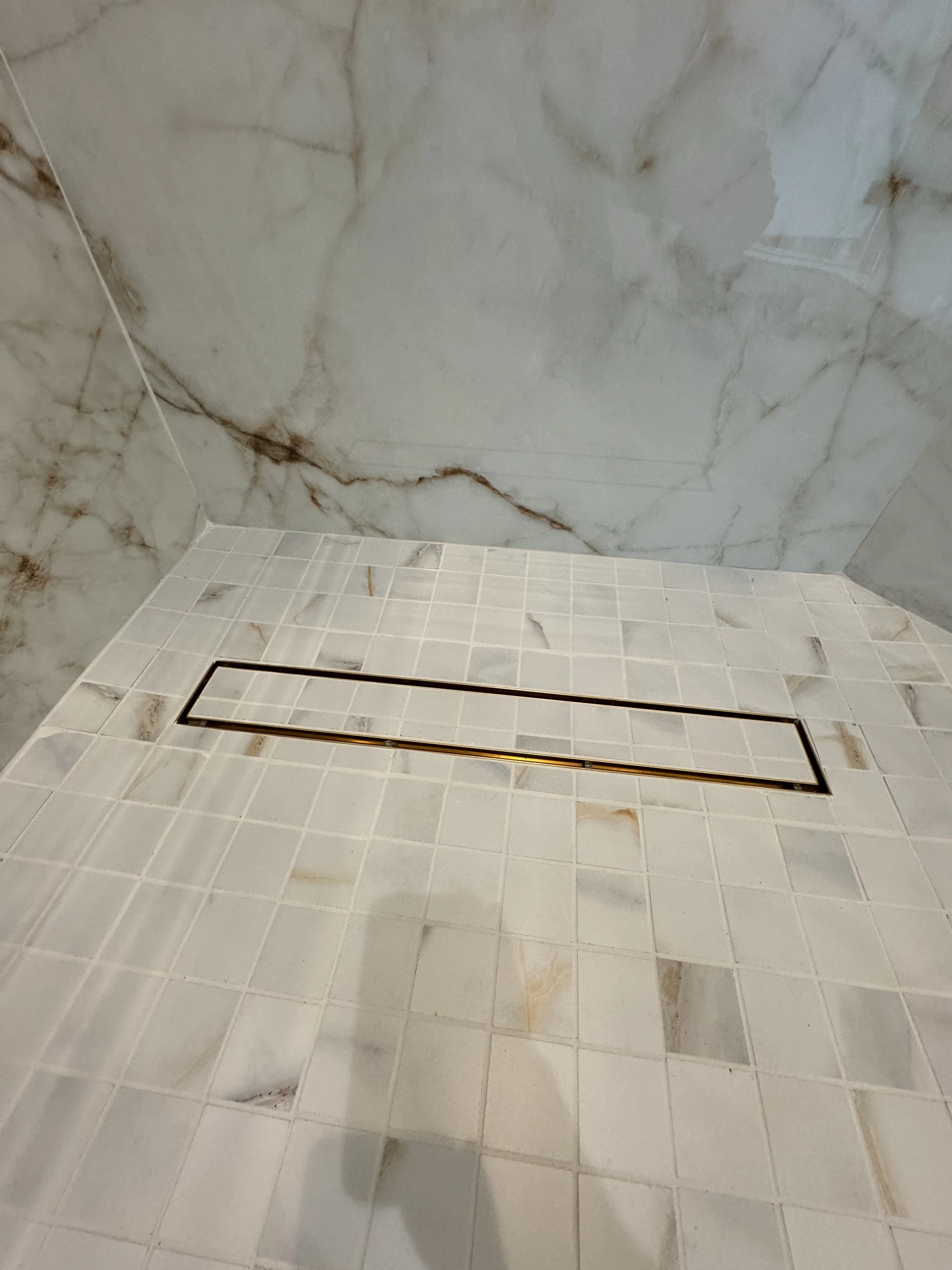 A marble bathroom shower with beige tiled floor and marble wall.