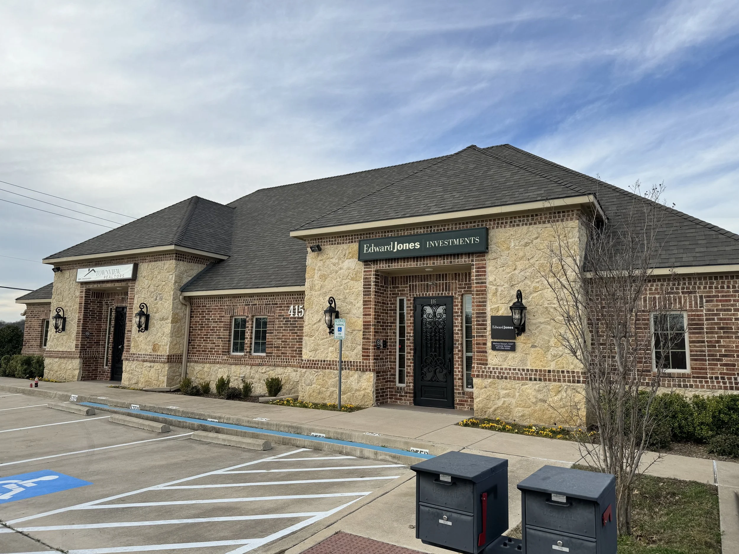 A commercial building with signs for Edward Jones Investments and TownView Realtors, featuring a parking lot with marked spaces and blue handicap spots, some small trees, and a cloudy sky above.