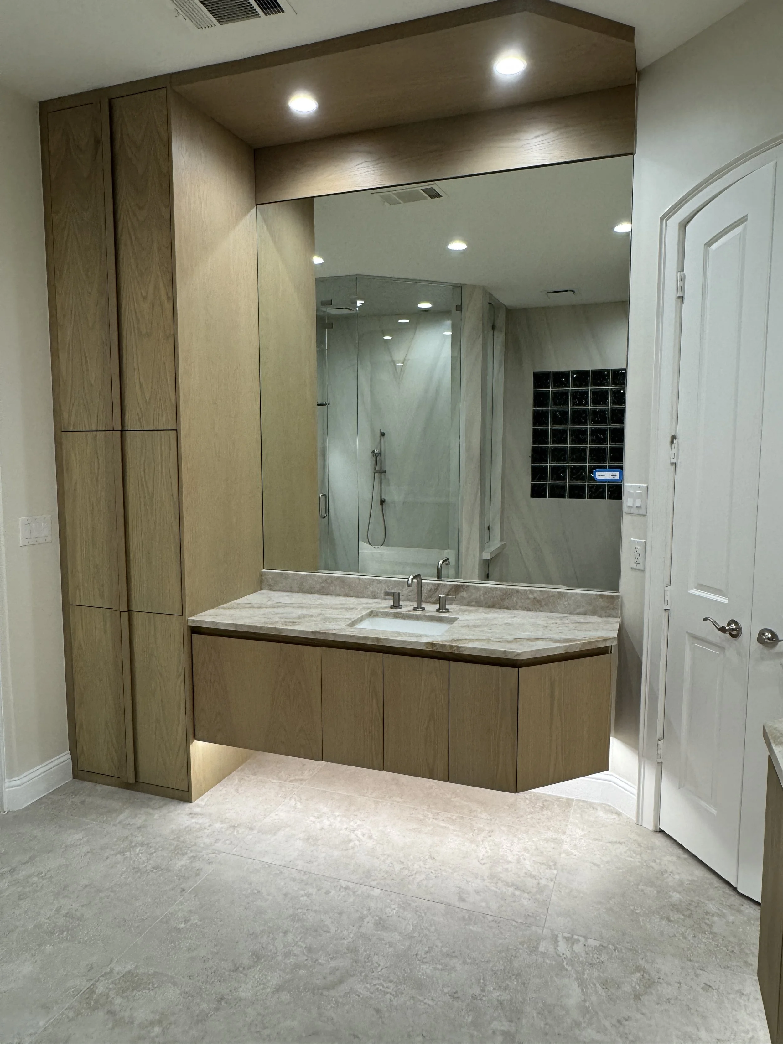 Bathroom with large mirror, wooden cabinetry, marble countertop, and glass shower enclosure.