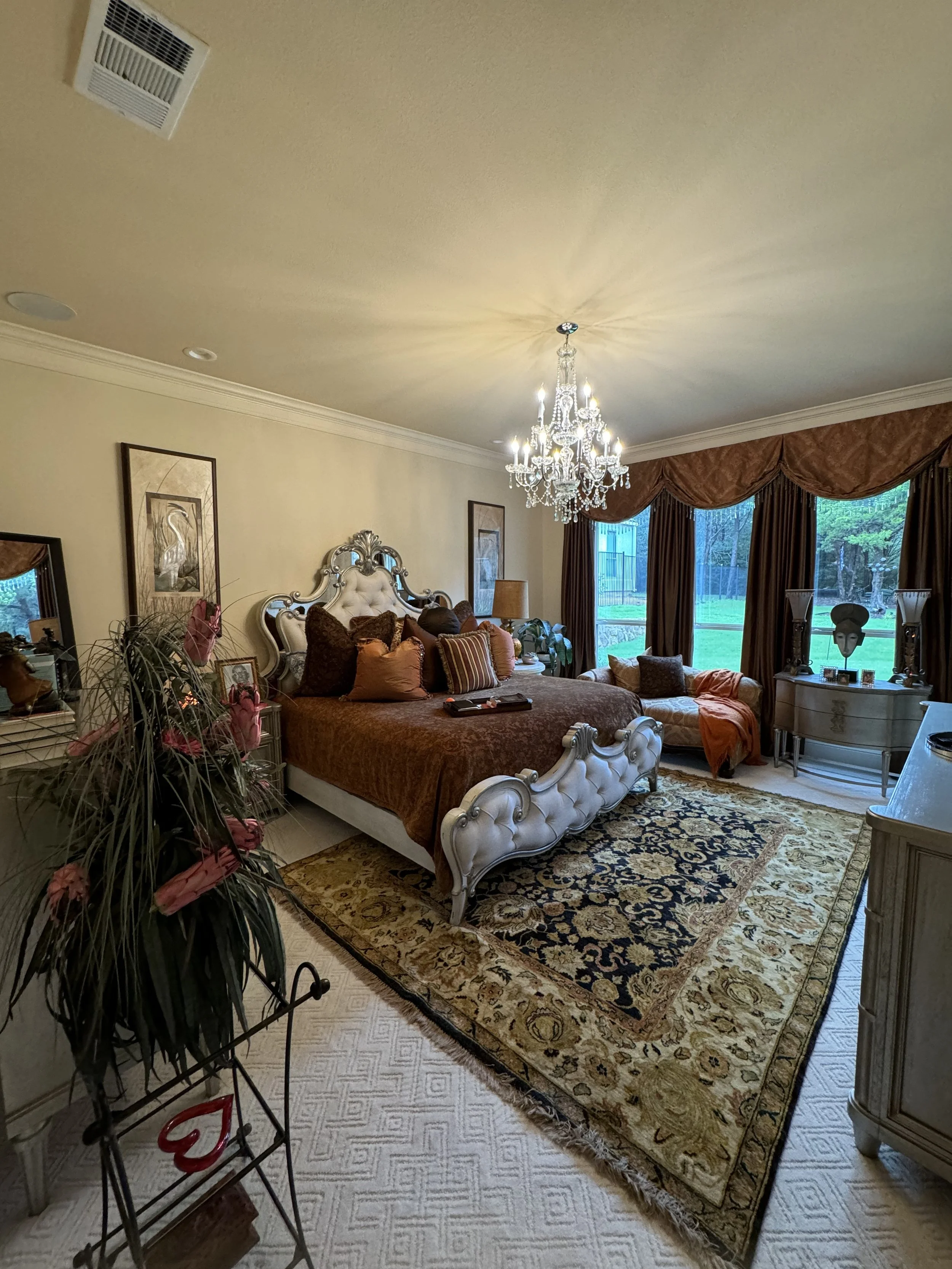 Living room with a bed, chandelier, large window with curtains, and various furniture and decorative items.
