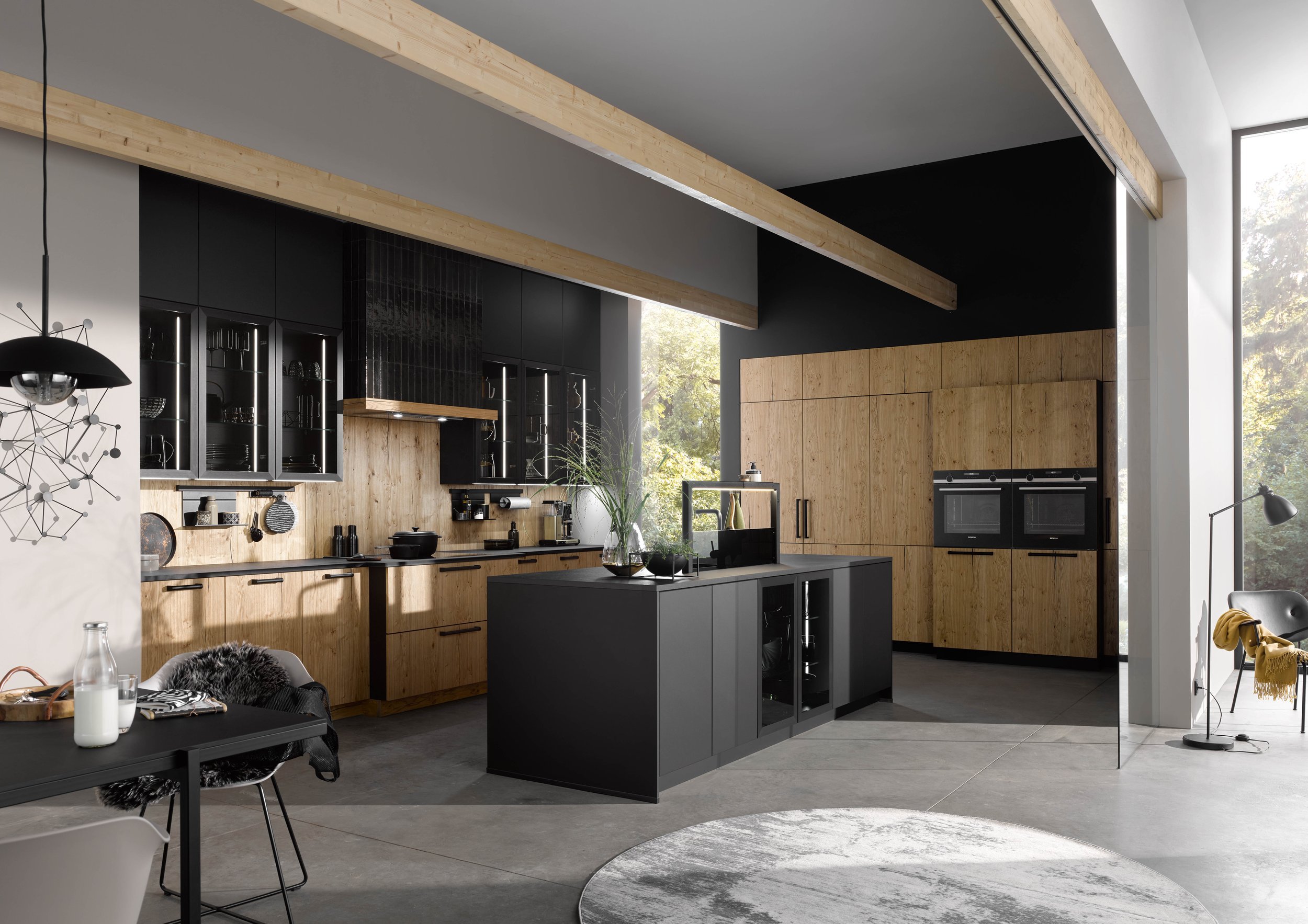 Modern kitchen with black and wooden cabinets, an island with a black countertop, large windows, a black oven, and minimalistic decor.