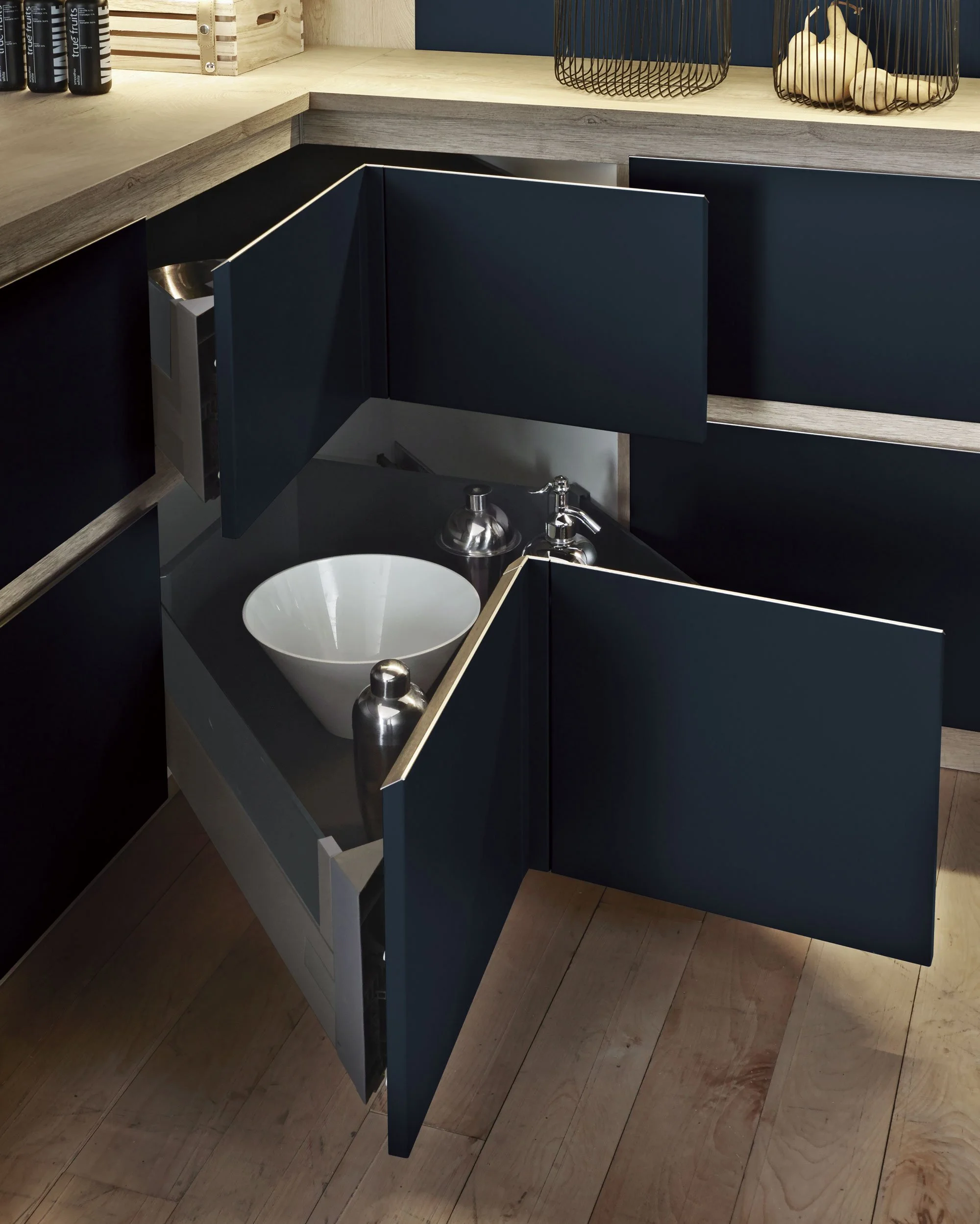 A kitchen corner with navy blue cabinets, a wooden countertop, and an open cabinet drawer revealing a white bowl, a metallic shaker, and a metallic soap dispenser.