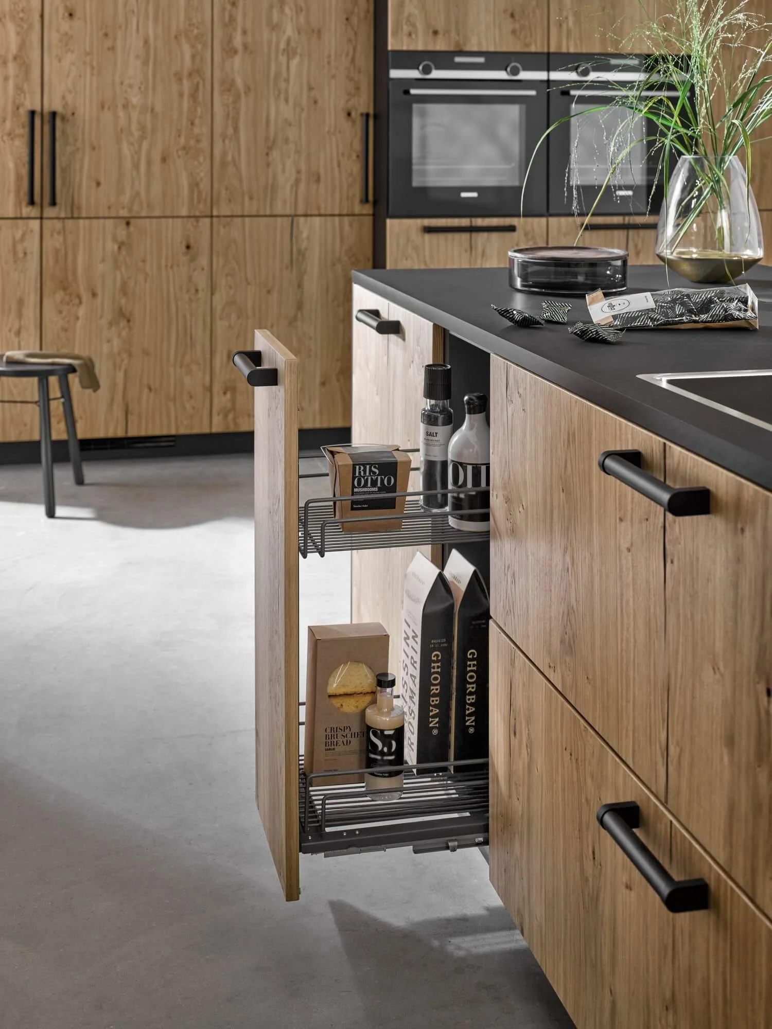 Open pull-out storage drawer in a modern kitchen with wood cabinetry, containing food items and kitchen supplies.