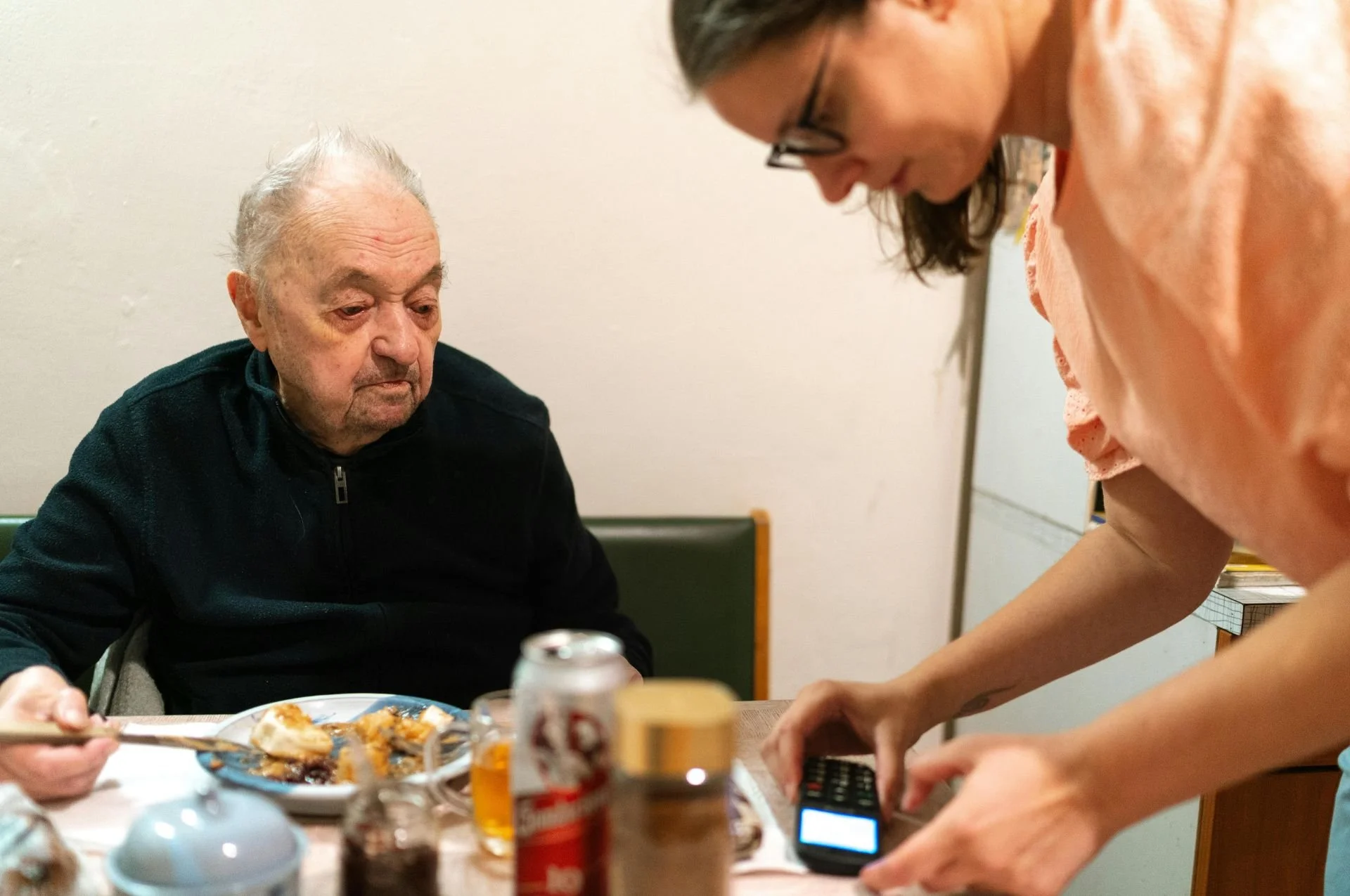 Older gentleman having breakfast while a younger person helps him set up his phone.