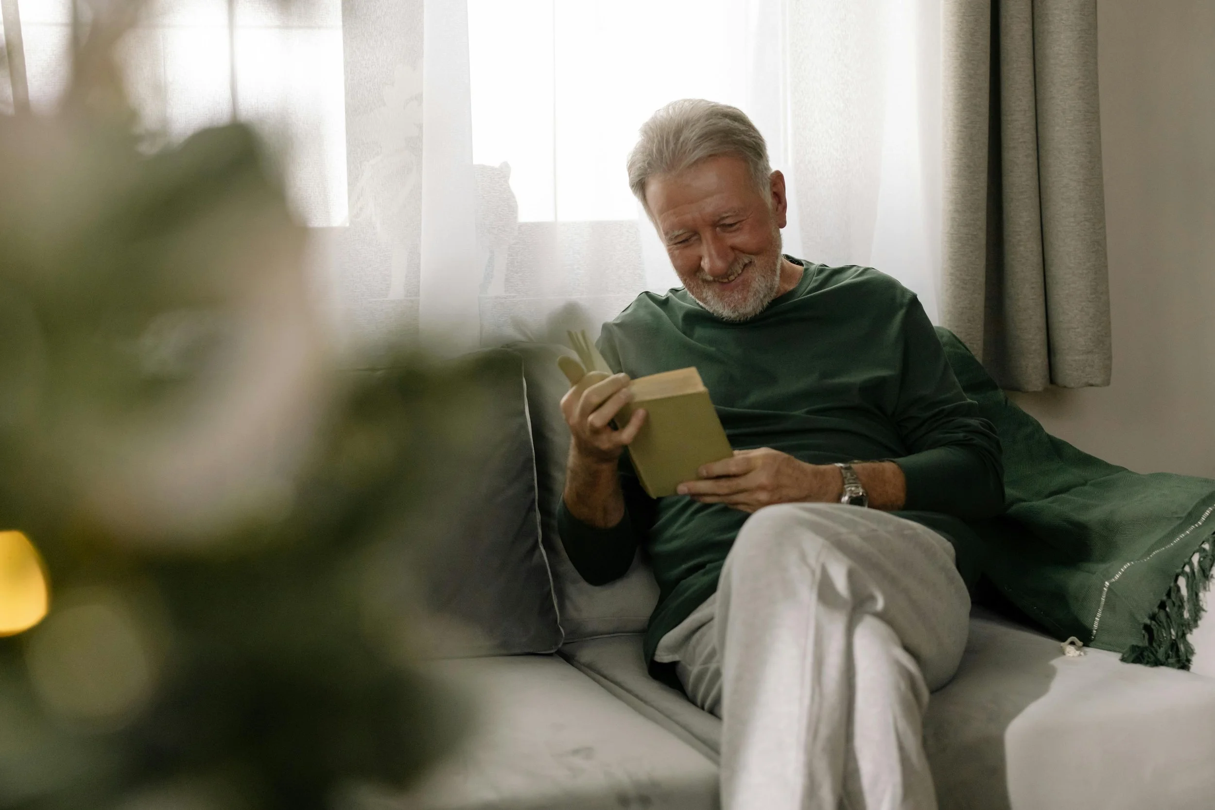 Senior man reading a book sittion on a sofa.