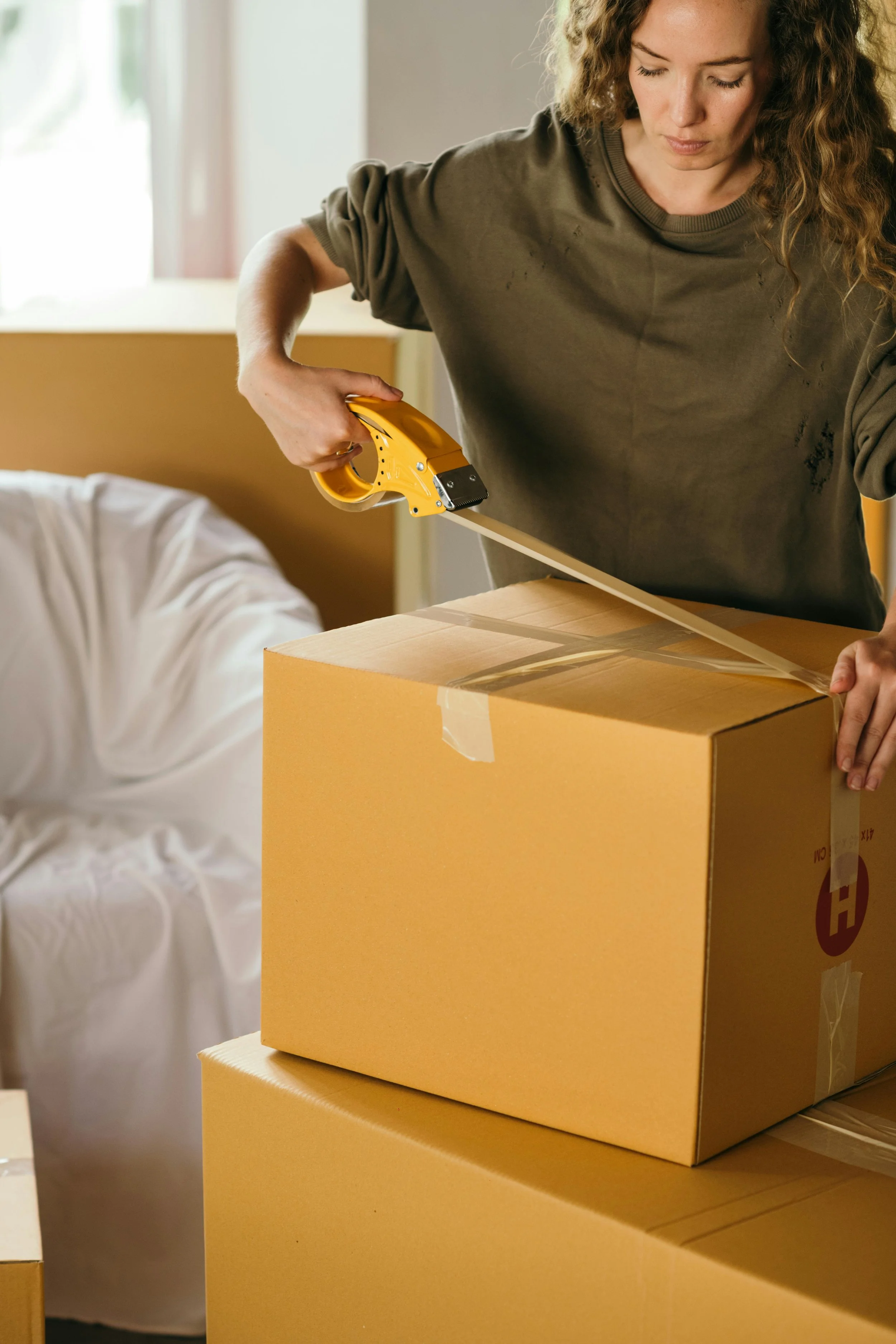 A woman is sealing a cardboard box with packing tape using a tape dispenser.