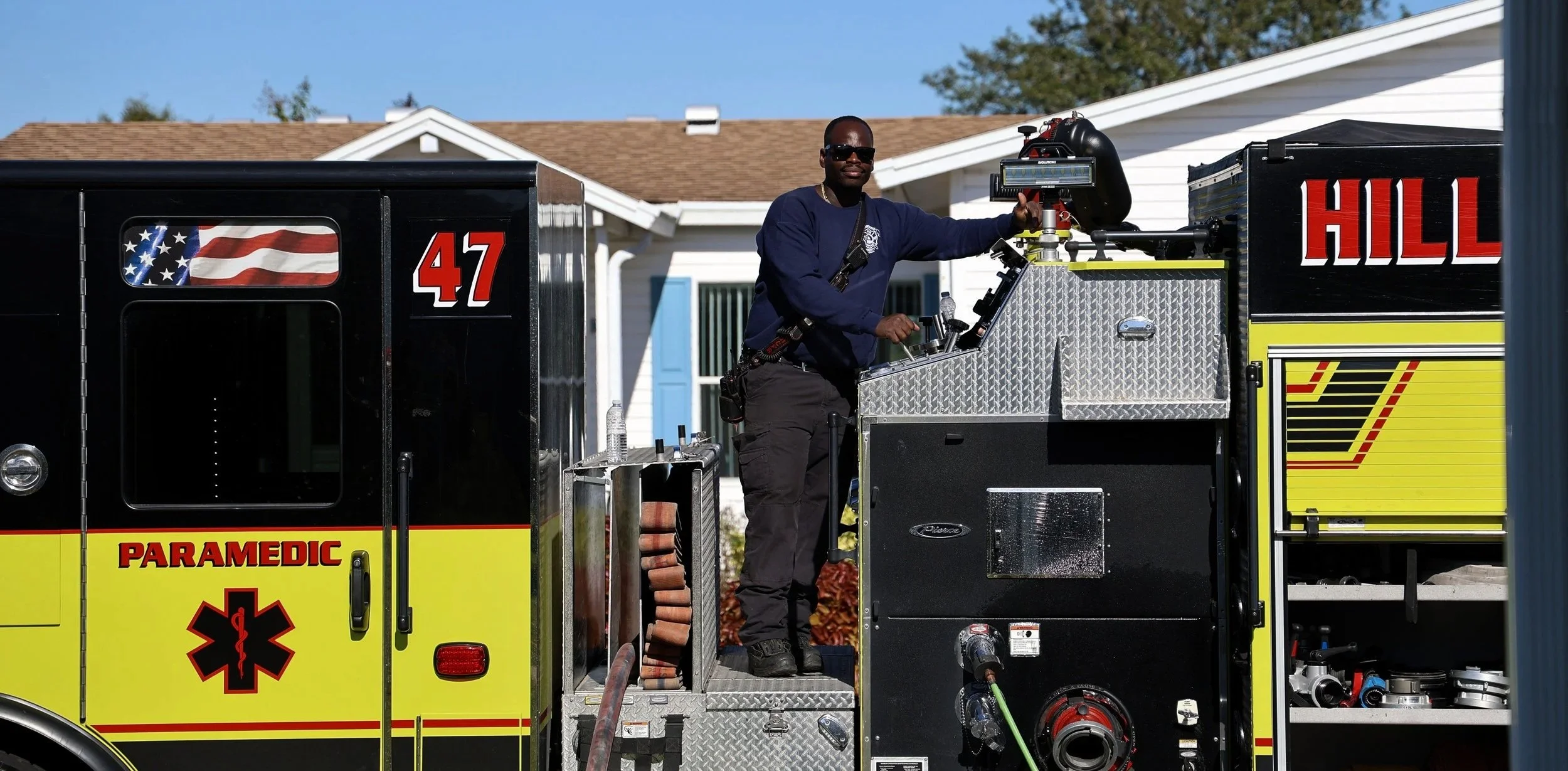 Firefighter carrying a ladder walking in front of a fire truck