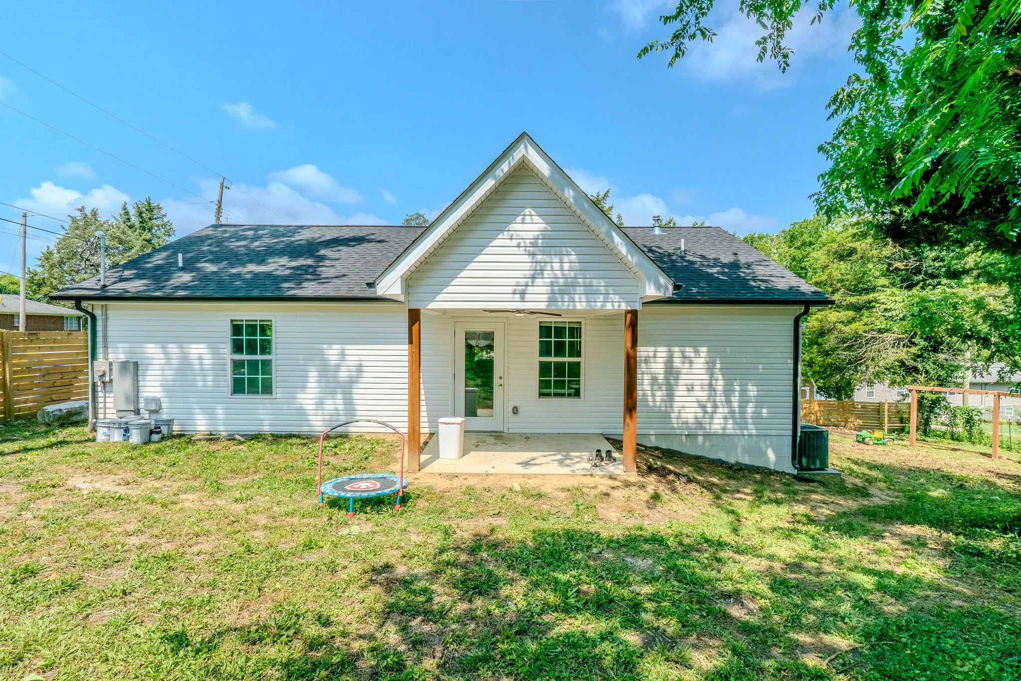 Backyard of a white house with a small porch, surrounded by grass and trees, with a blue sky and some clouds.