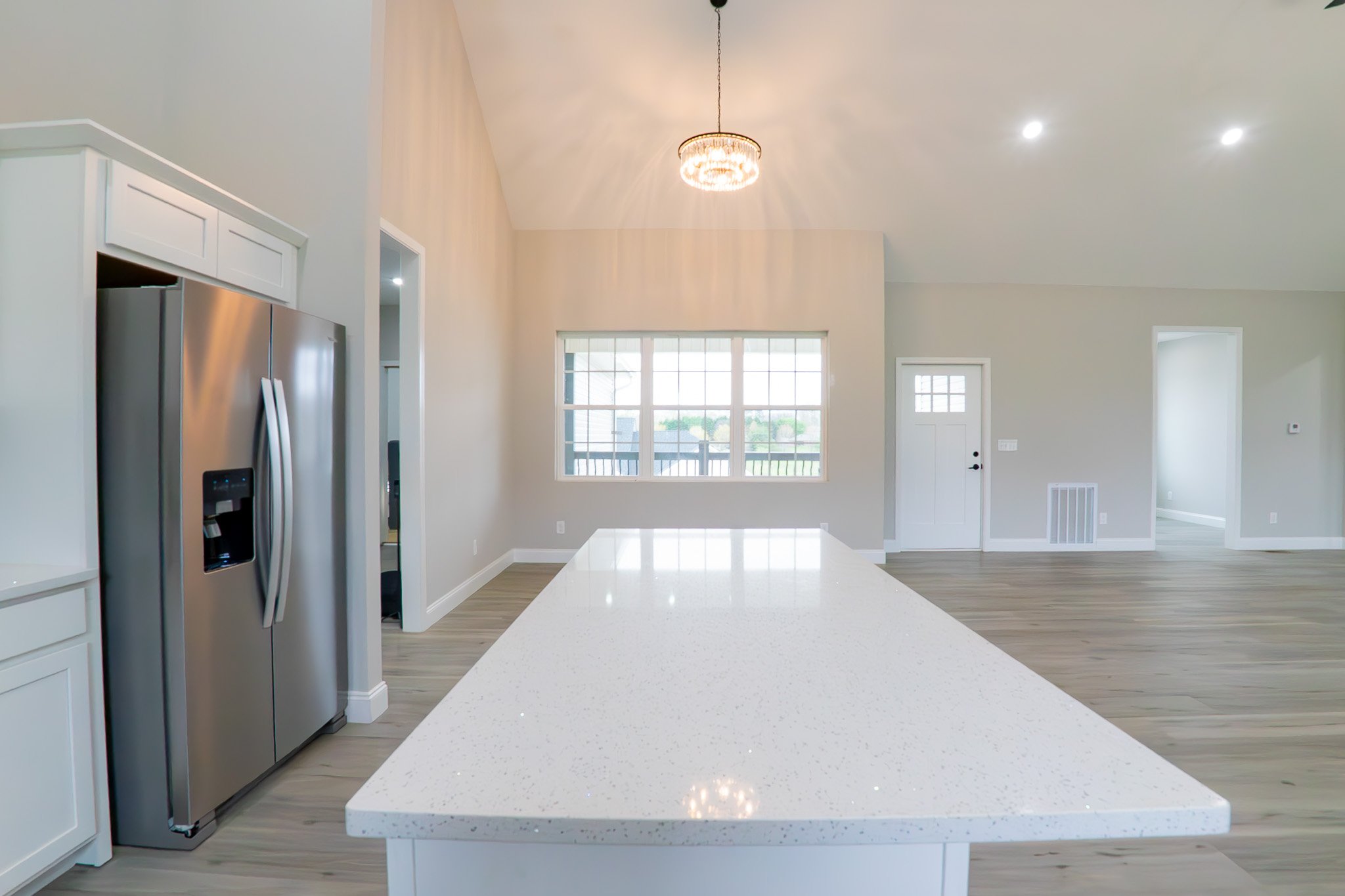 Modern kitchen interior with stainless steel appliances, large white countertop, pendant light, and light hardwood floors.