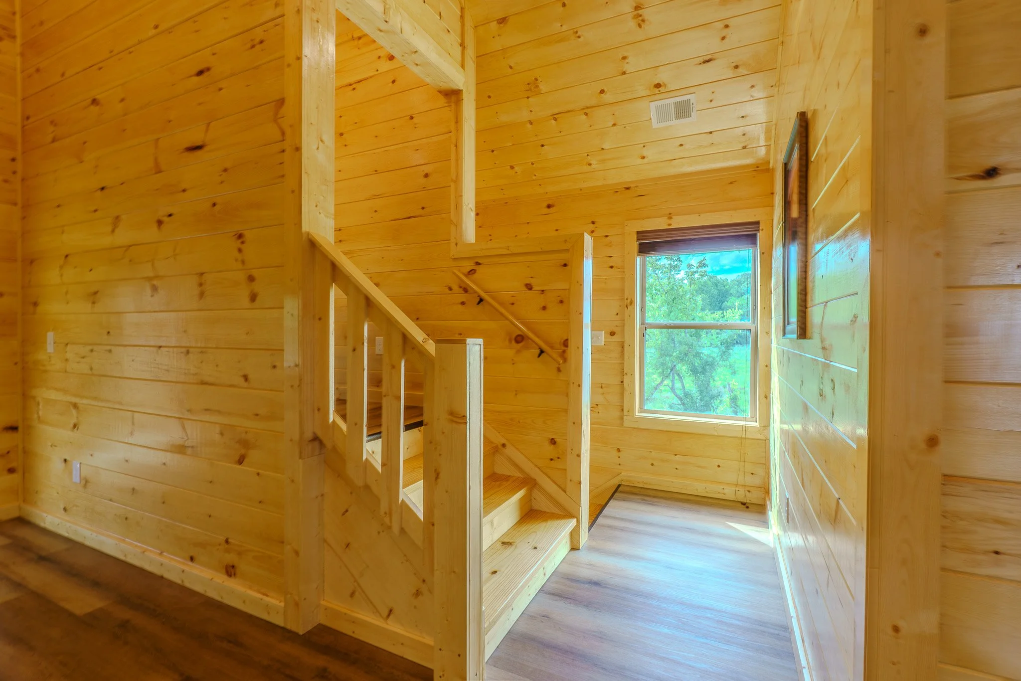 Interior view of a wooden staircase with a window showing trees outside.