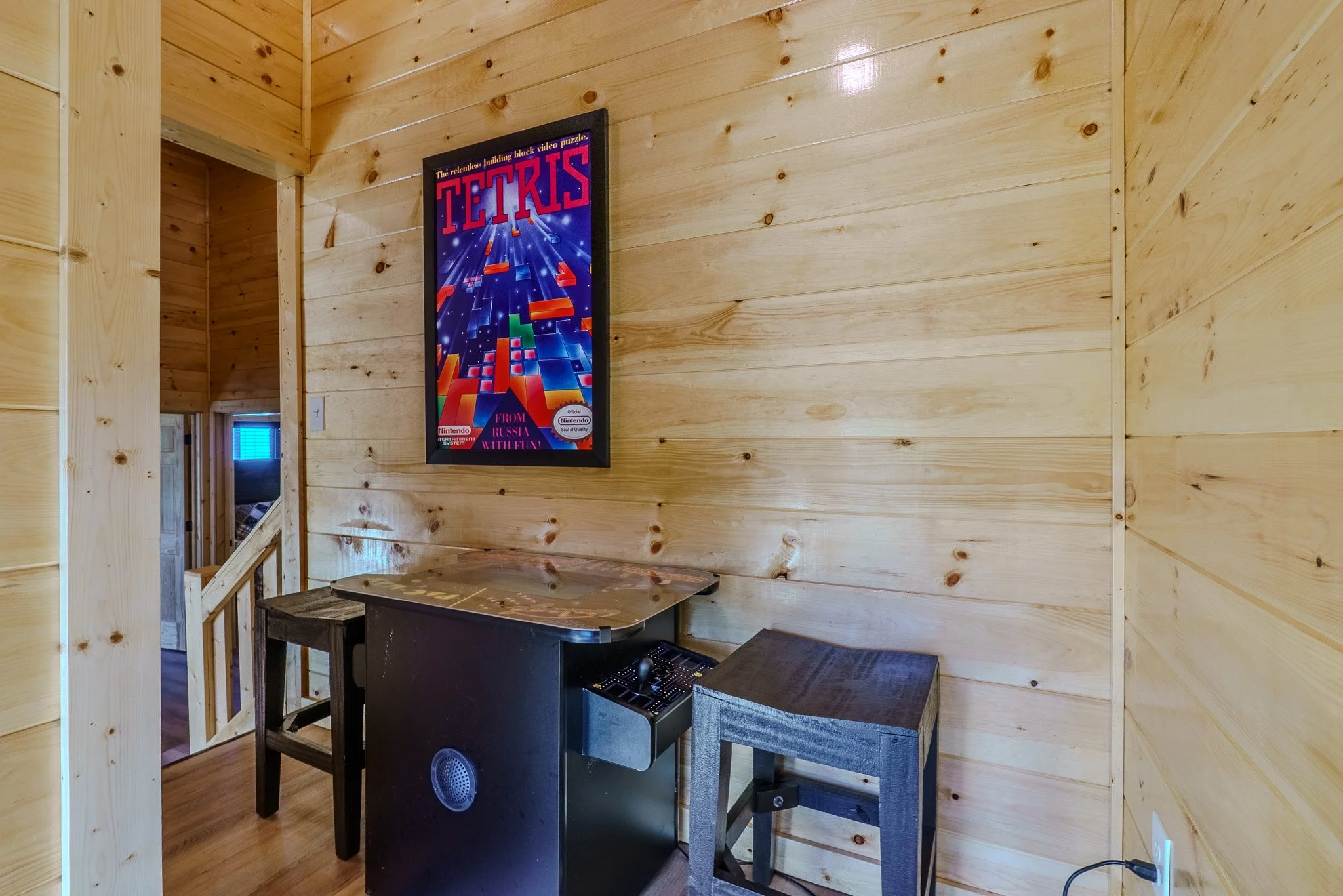 Wood-paneled room with a Tetris poster on the wall, a small black table with a map on it, a black chair, and a gray wooden stool.