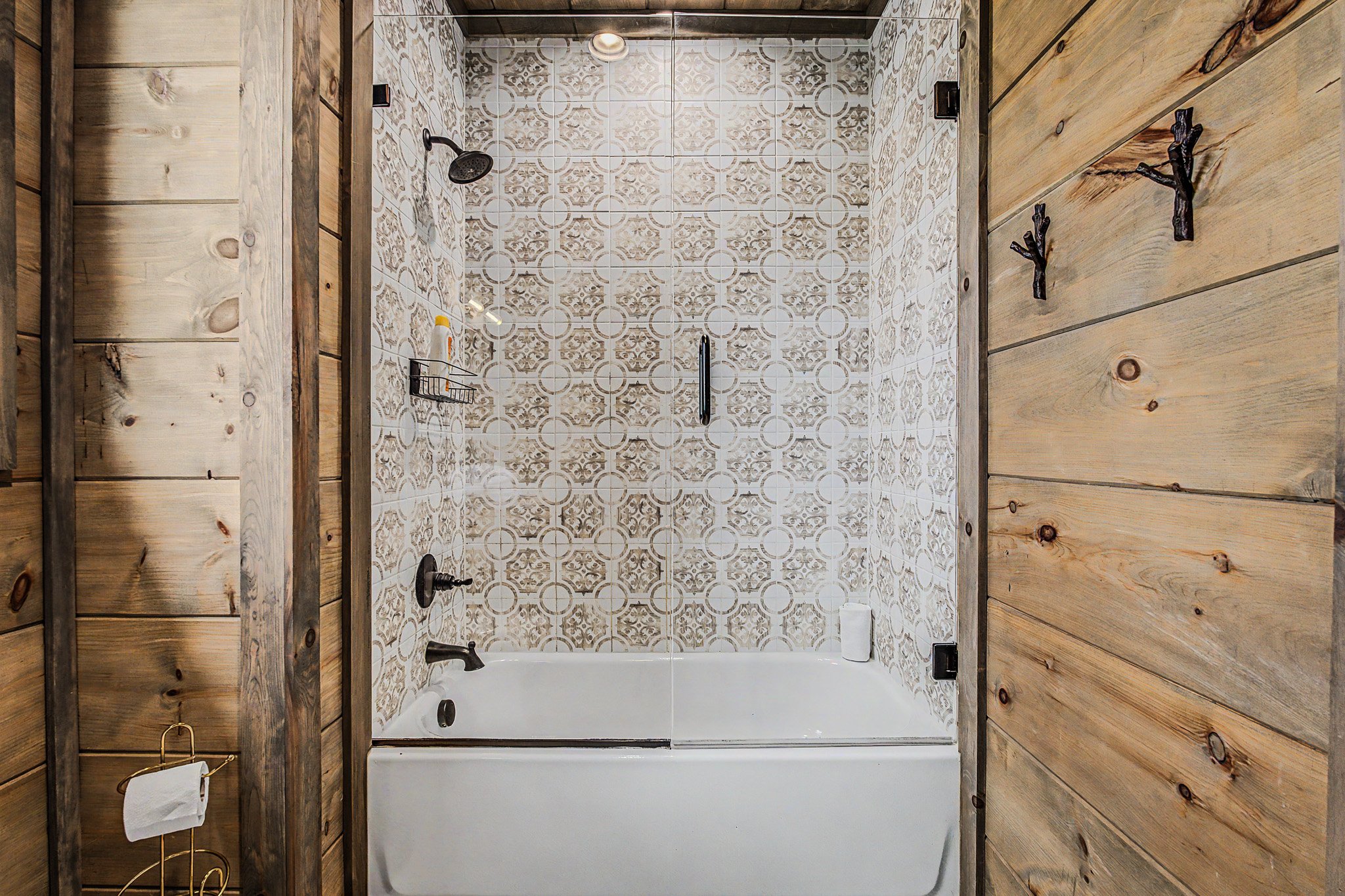 Overhead view of a rustic bathroom with a bathtub, wooden walls, and decorative tile flooring.