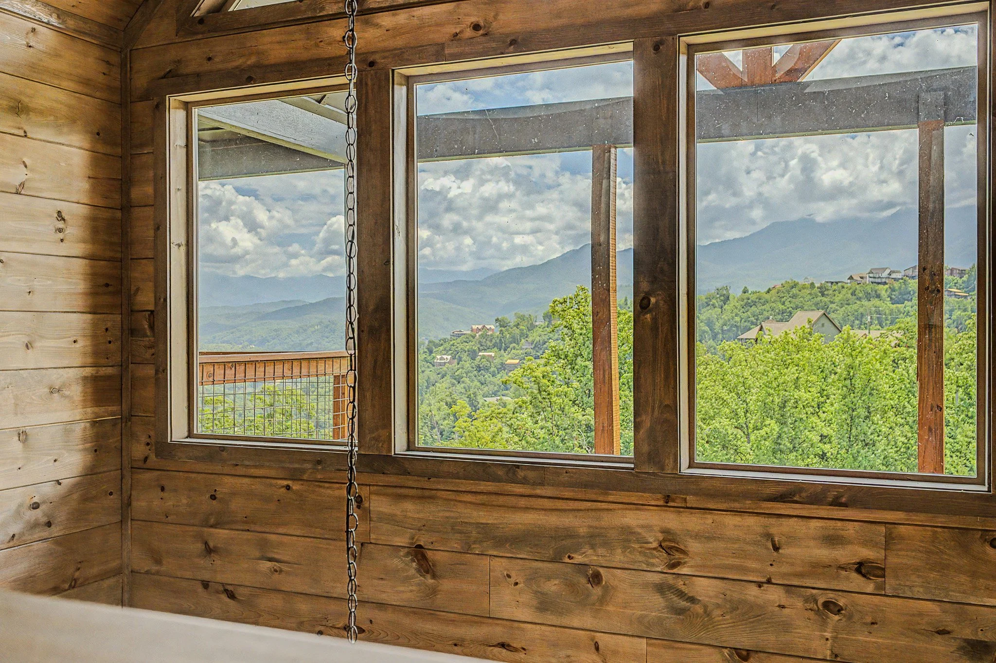 View of mountains and greenery through large window with wooden frame and partial mountain construction support beams inside a room with wooden panel walls.