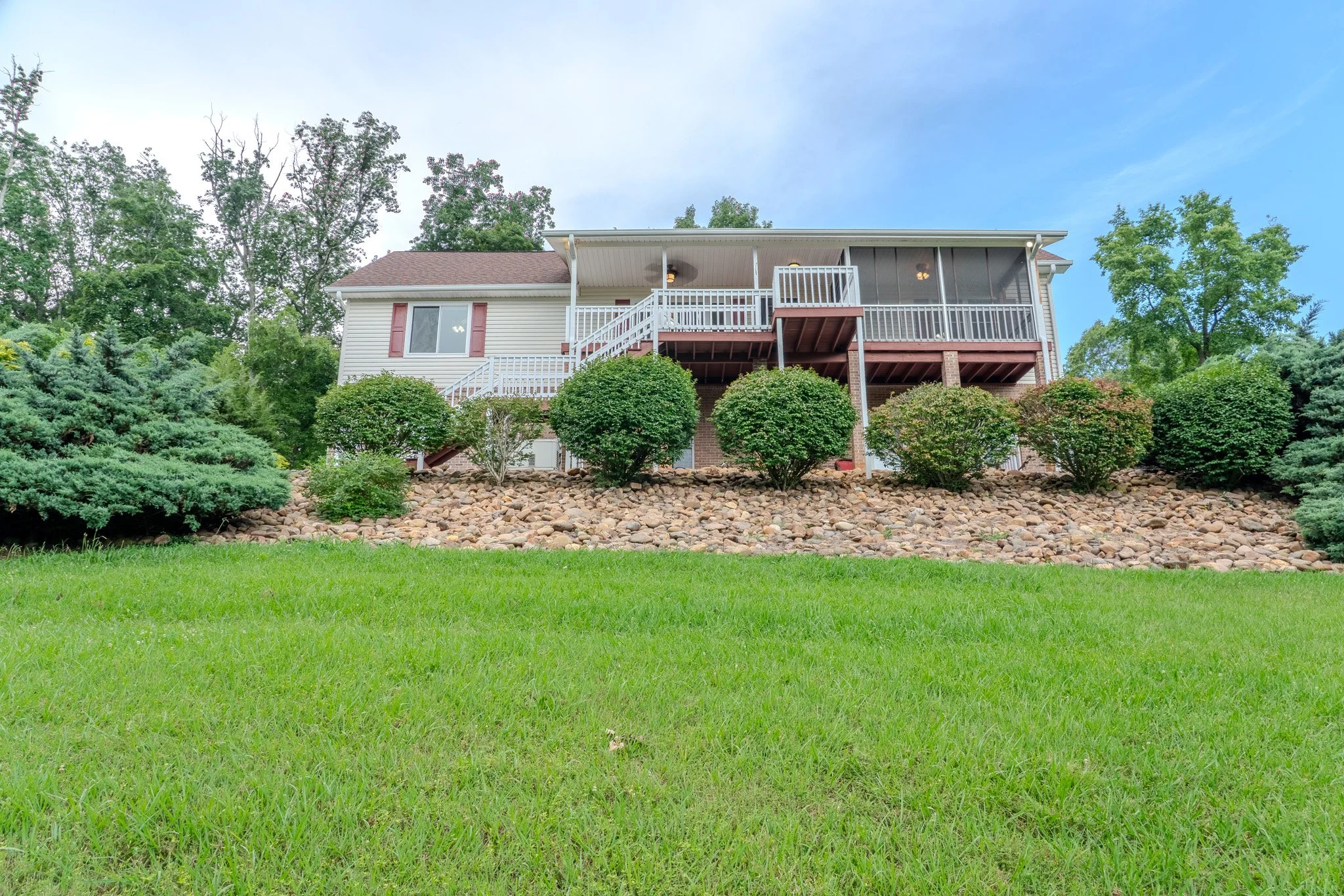 A house with a large backyard, featuring a lawn, rocks, bushes, and trees, photographed from the ground level looking upward.