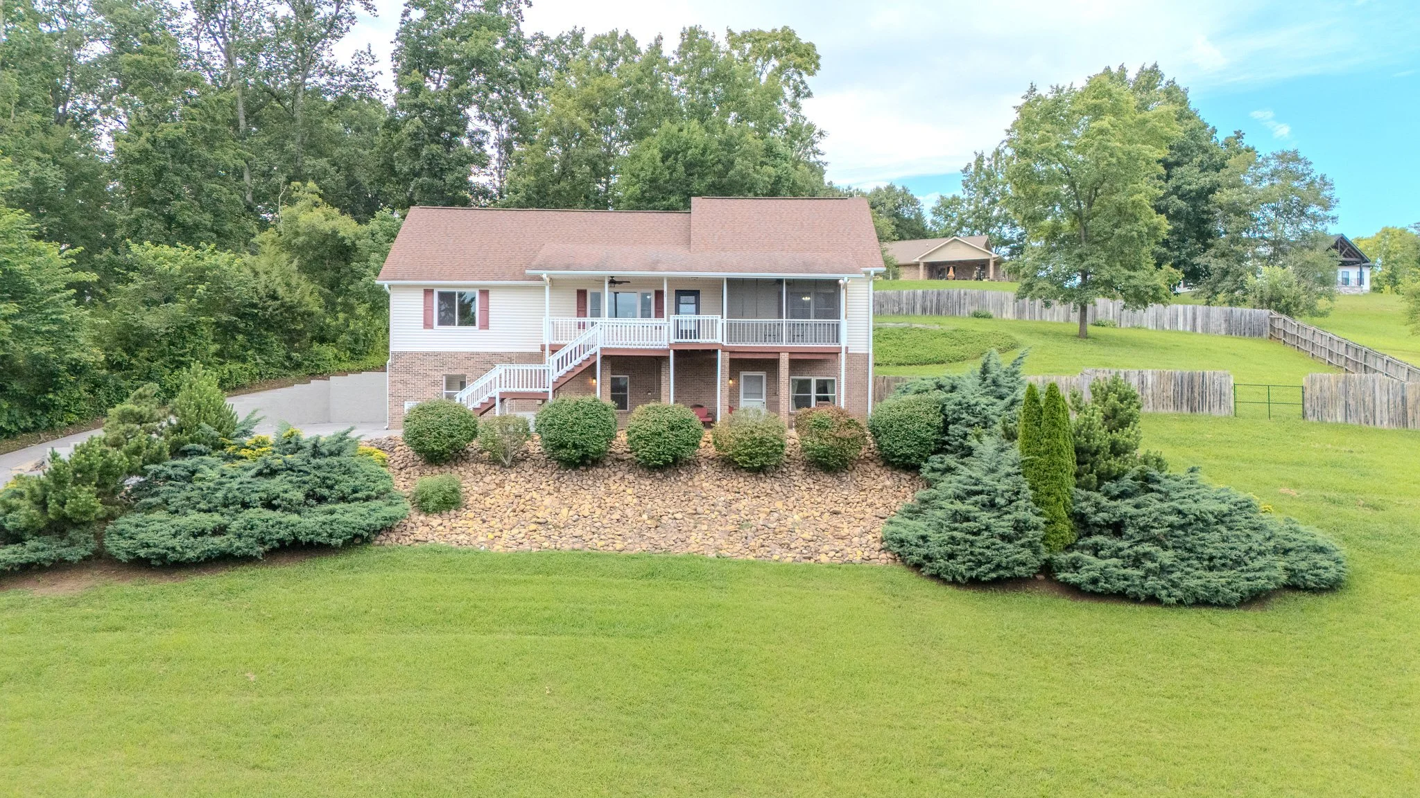 Front view of a two-story house with a screened porch and landscaped yard surrounded by trees and wooden fences.