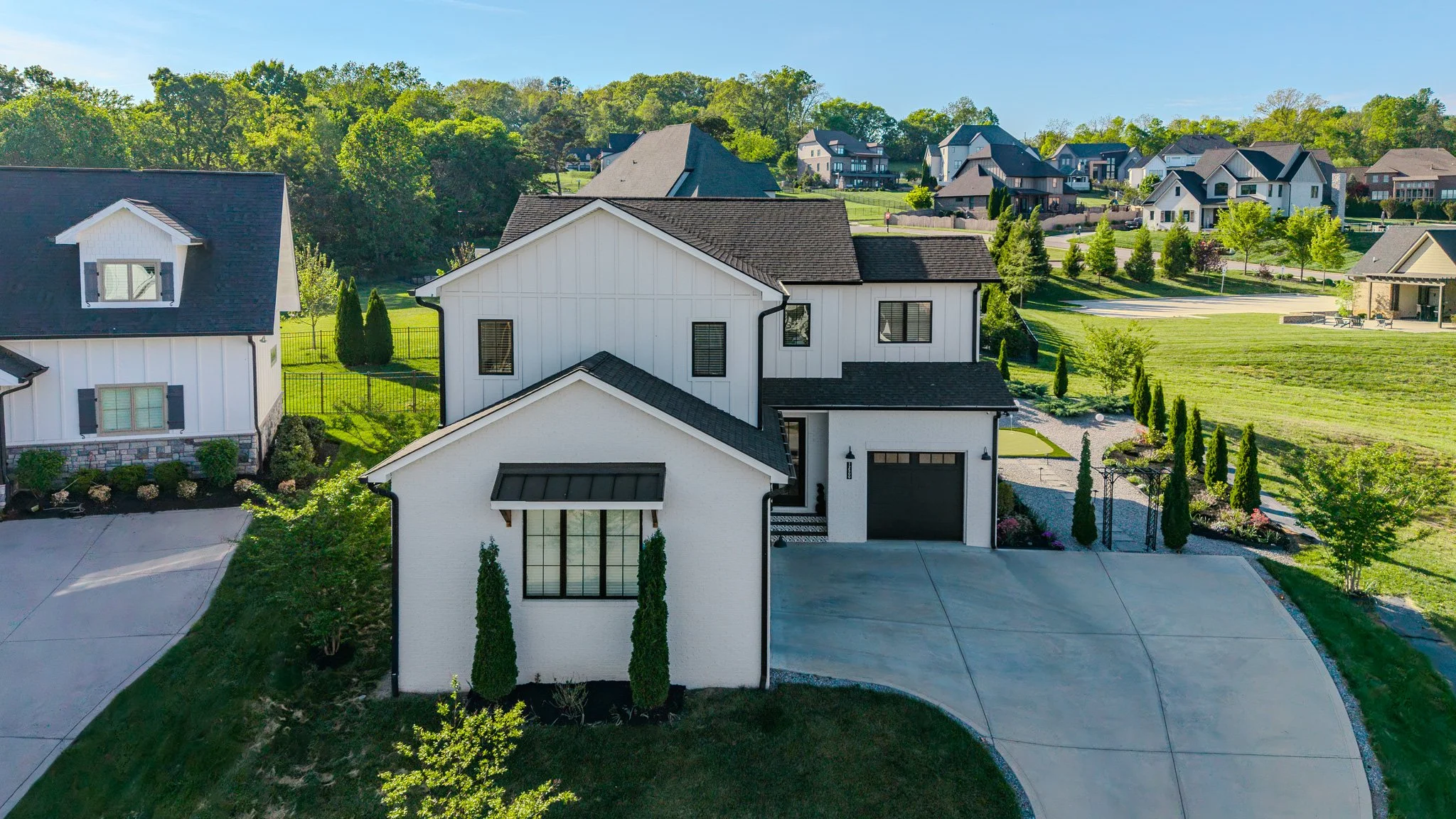 A modern white house with black accents, surrounded by greenery, in a suburban neighborhood.