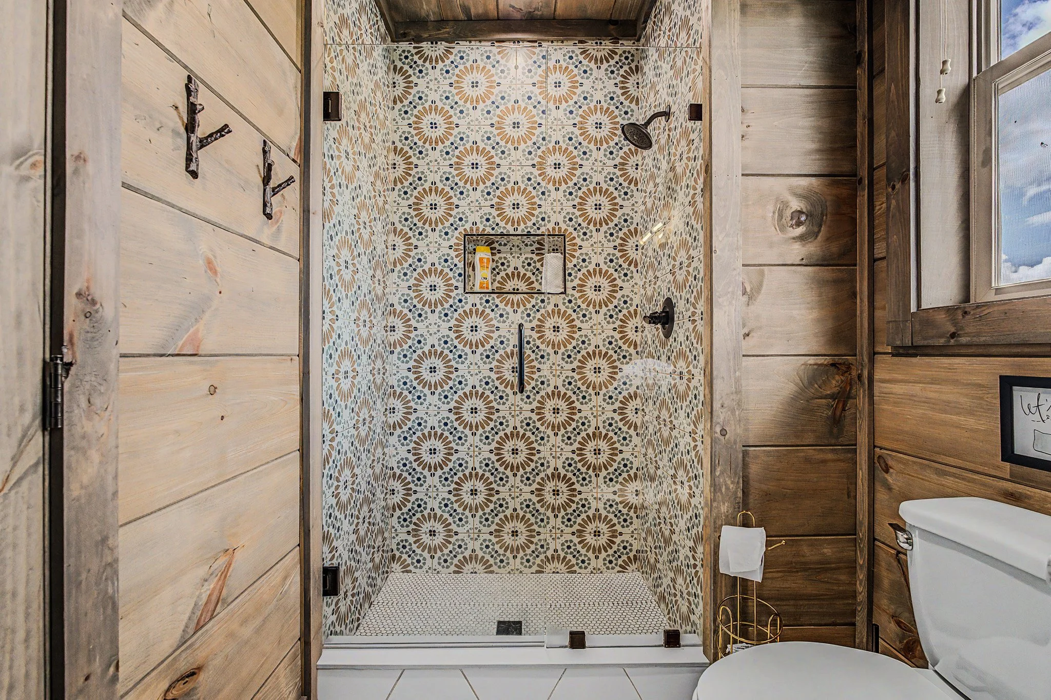 Bathroom with patterned tile shower, wooden walls, and a toilet.