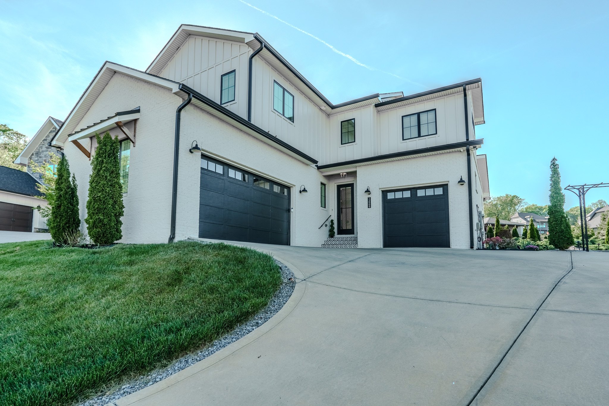 A modern two-story house with white and black exterior, two garage doors, a front door with steps, and manicured lawn with shrubbery.