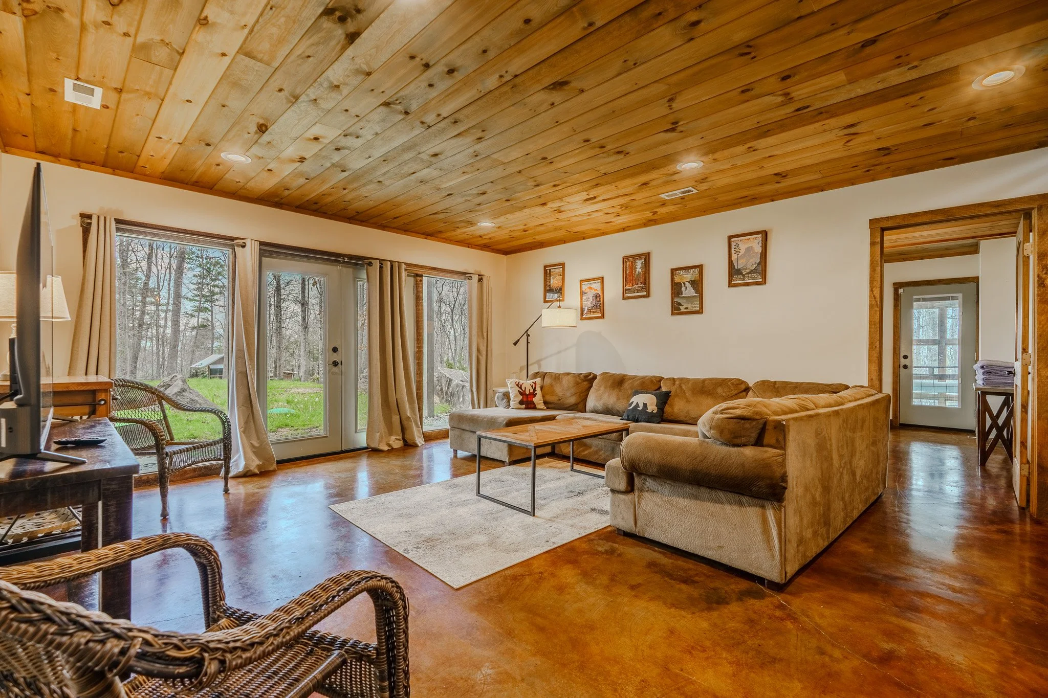 Living room with large sectional sofa, wooden coffee table, and sliding glass doors leading to outdoor area with trees.