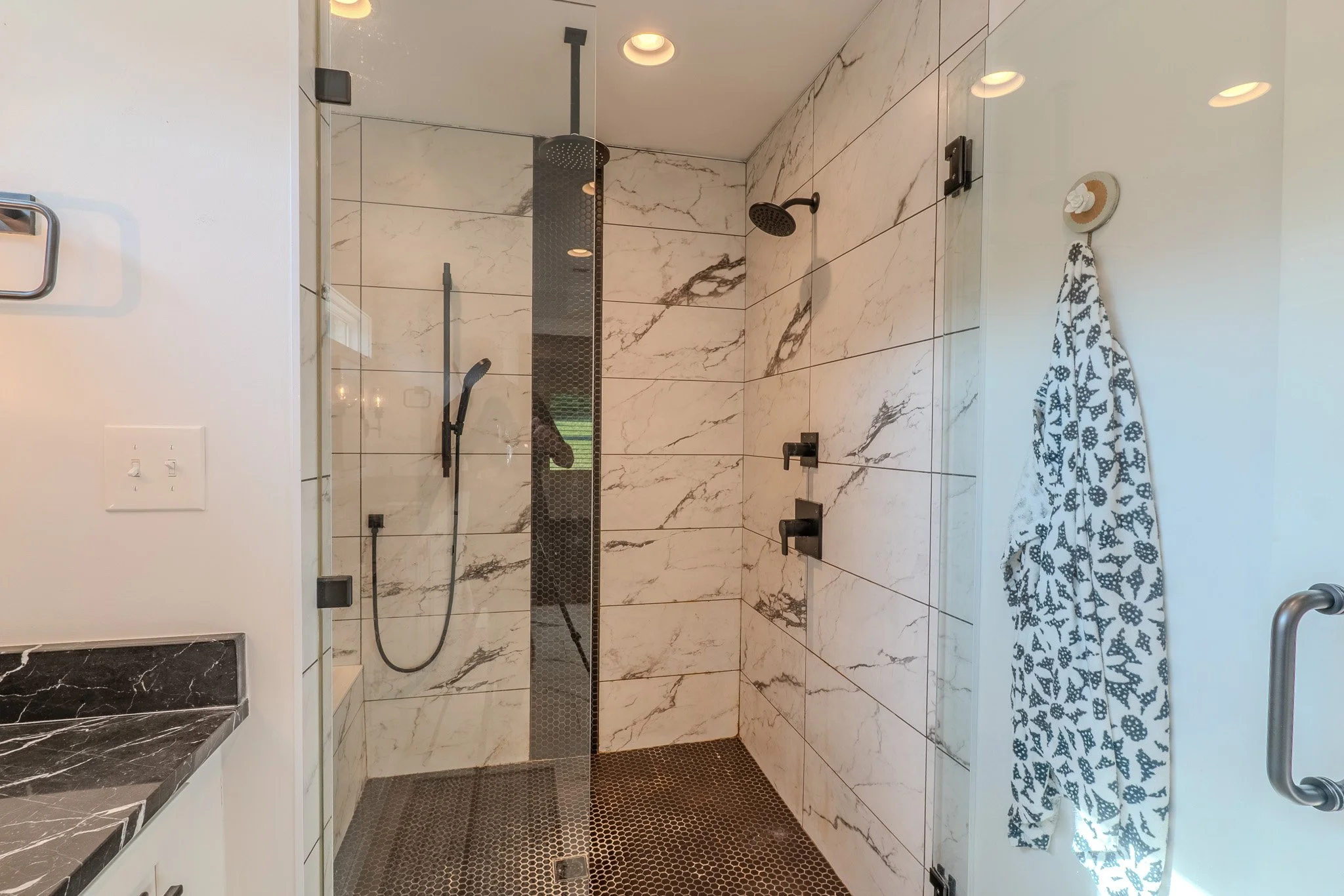 Modern glass-enclosed shower with black fixtures, marble tiles, and a patterned towel hanging on a hook.