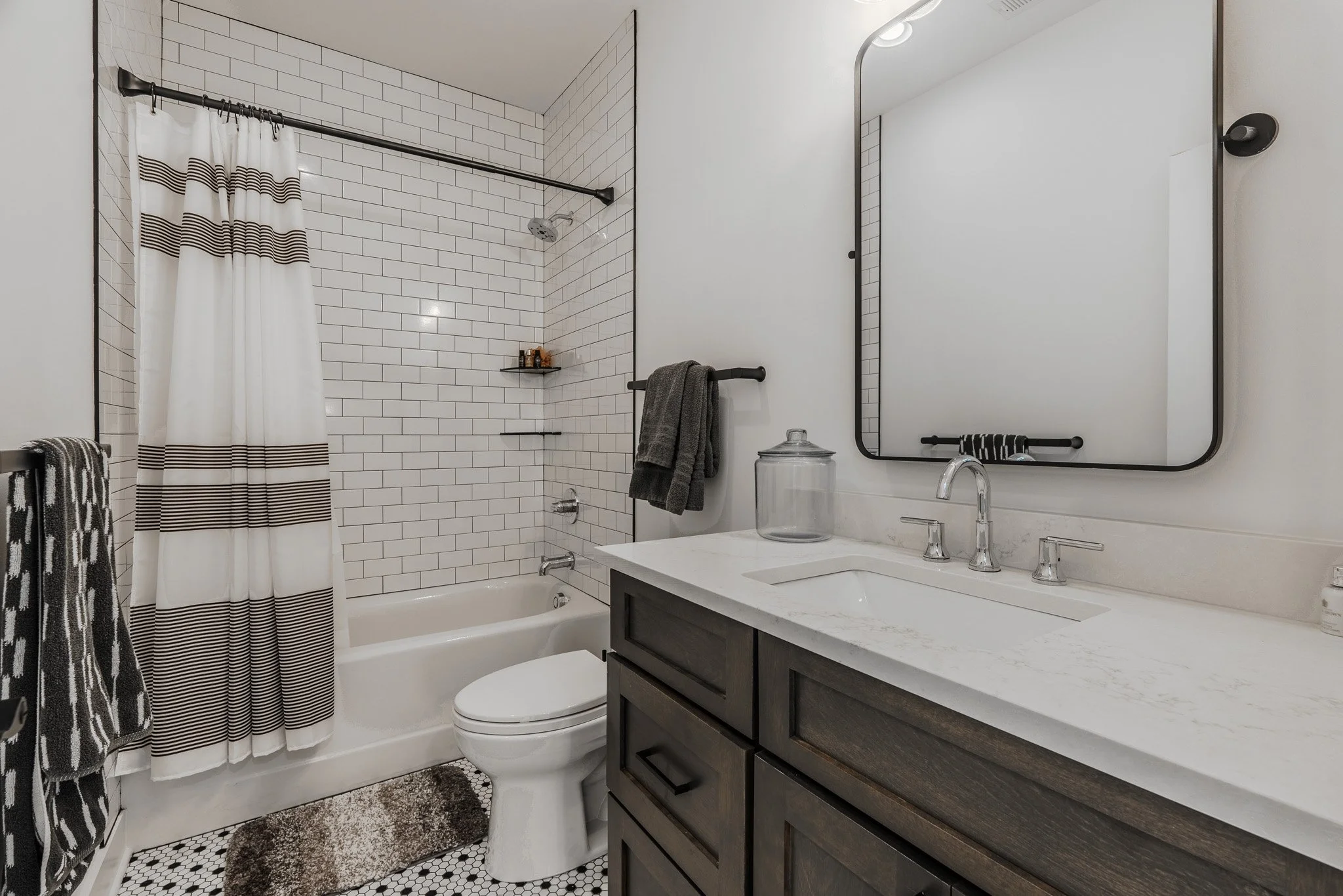 Modern bathroom with white subway tile shower, dark wood vanity with white marble countertop, and large wall mirror.