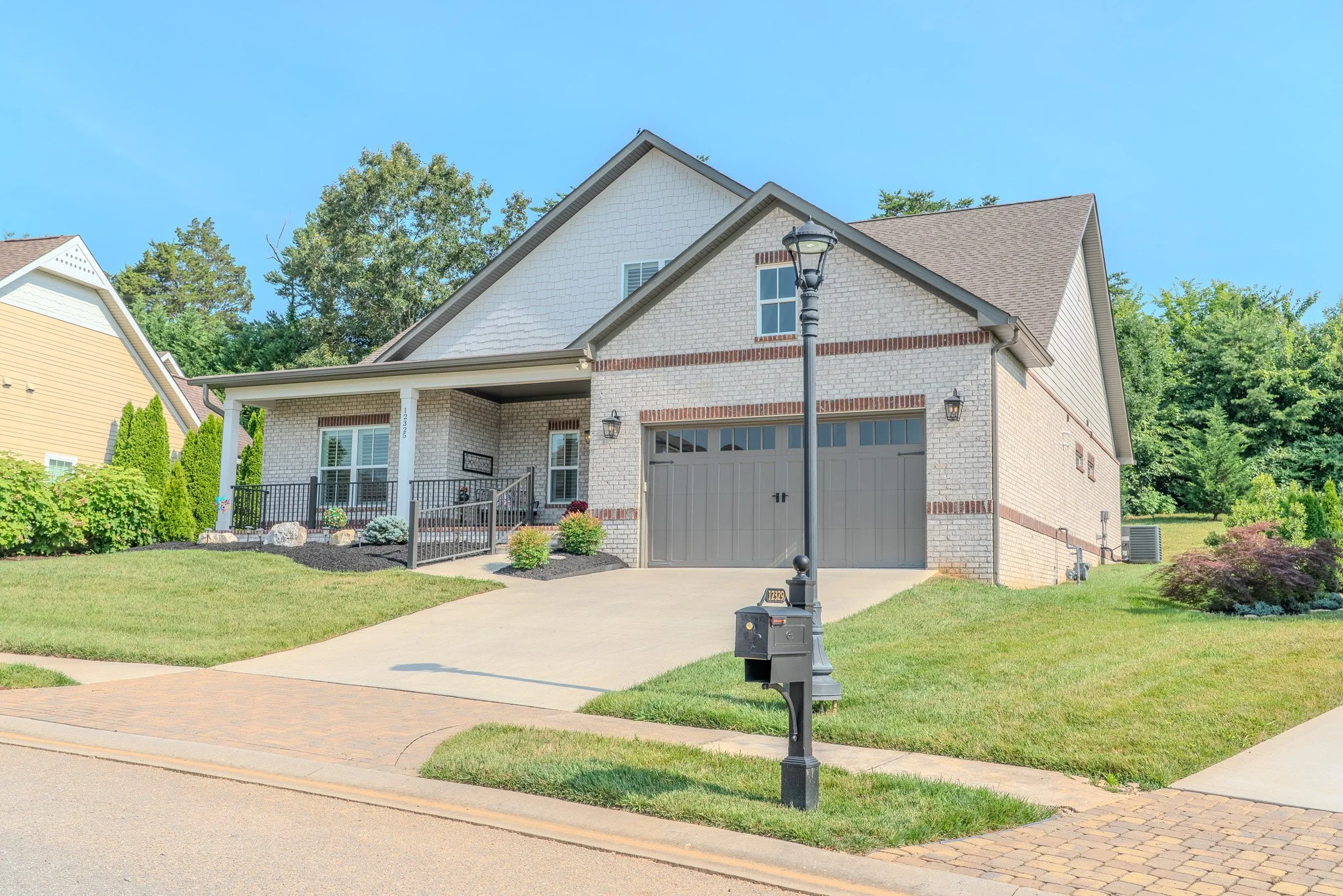 Front view of a two-story suburban house with a brick and siding exterior, a garage, landscaped lawn, driveway, and a black mailbox and street lamp in front.
